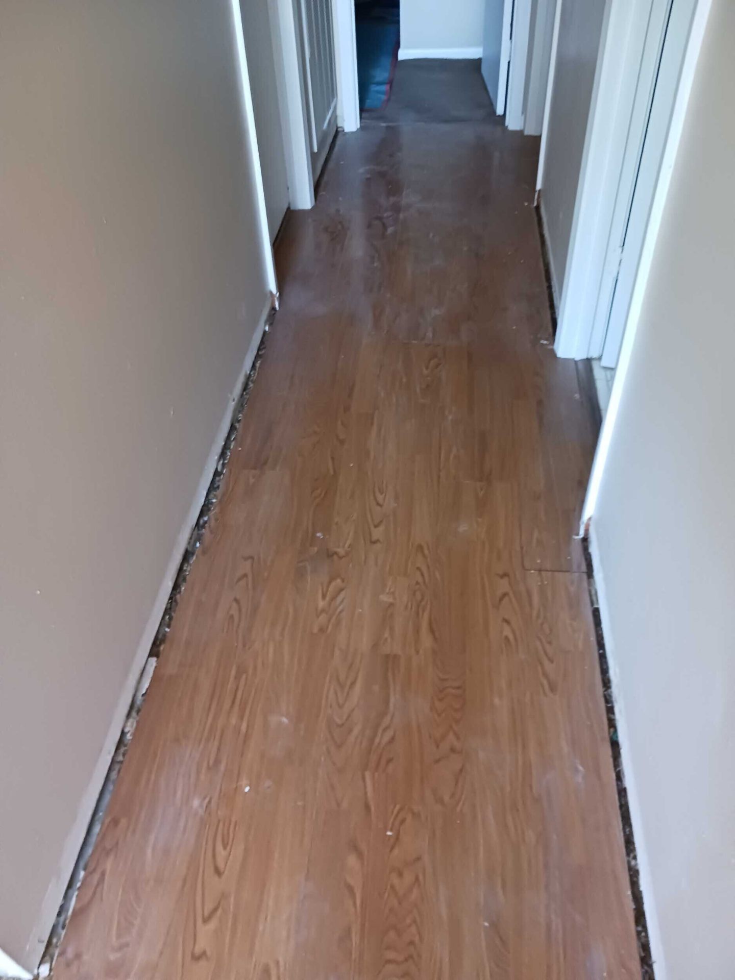 Hallway in the Gretna insurance repair with baseboards removed and existing laminate flooring pulled back to prep for new flooring throughout