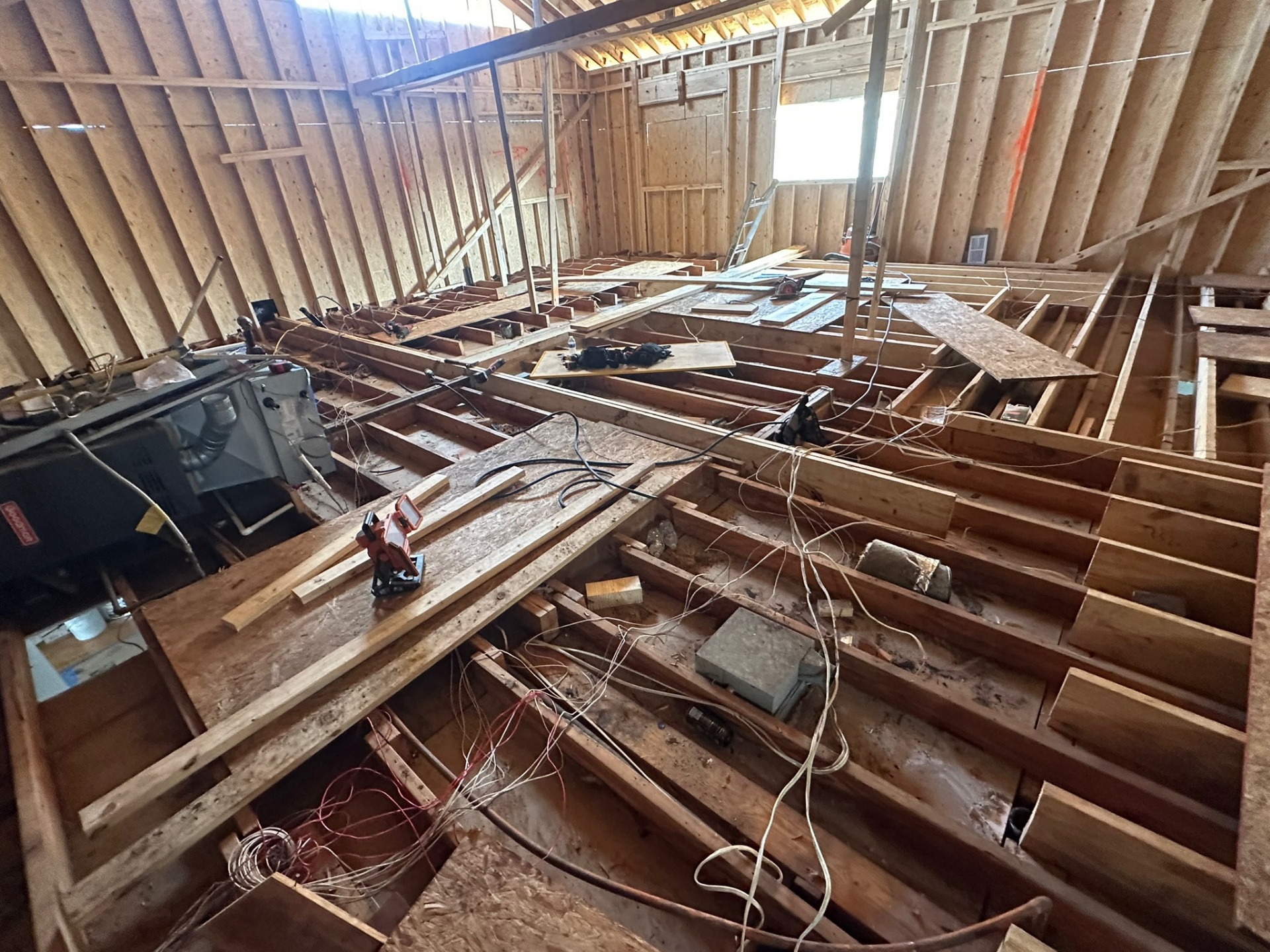 Wide overhead view of exposed floor joists inside Metairie attic with mechanical equipment and old wiring before new second-floor decking goes down