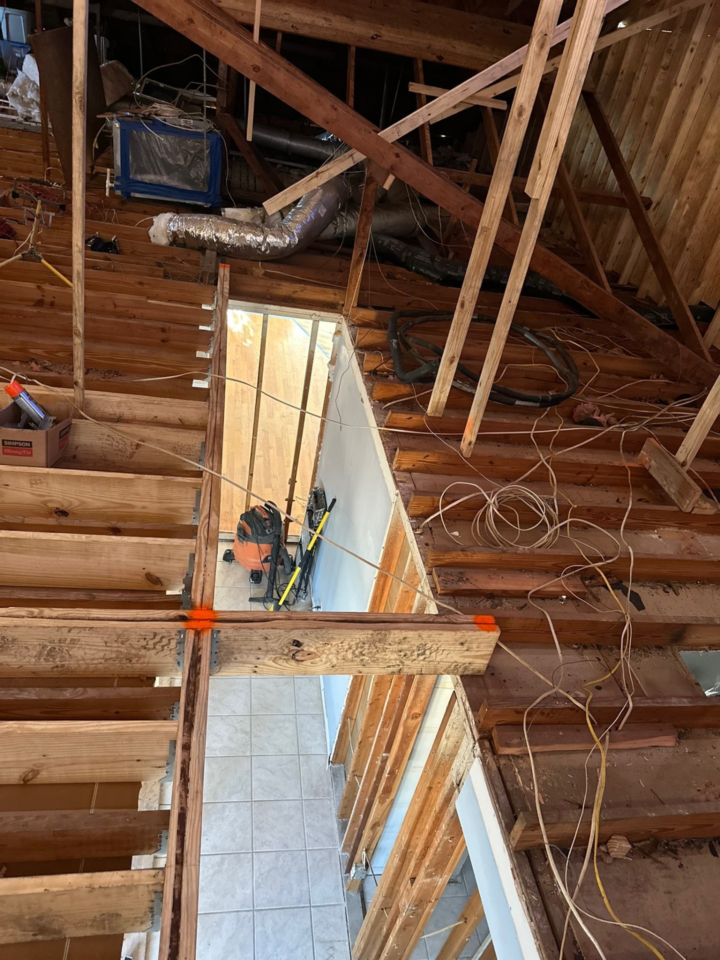 Overhead view through future stair opening showing new second-floor joists with Simpson Strong-Tie connectors over Metairie first floor