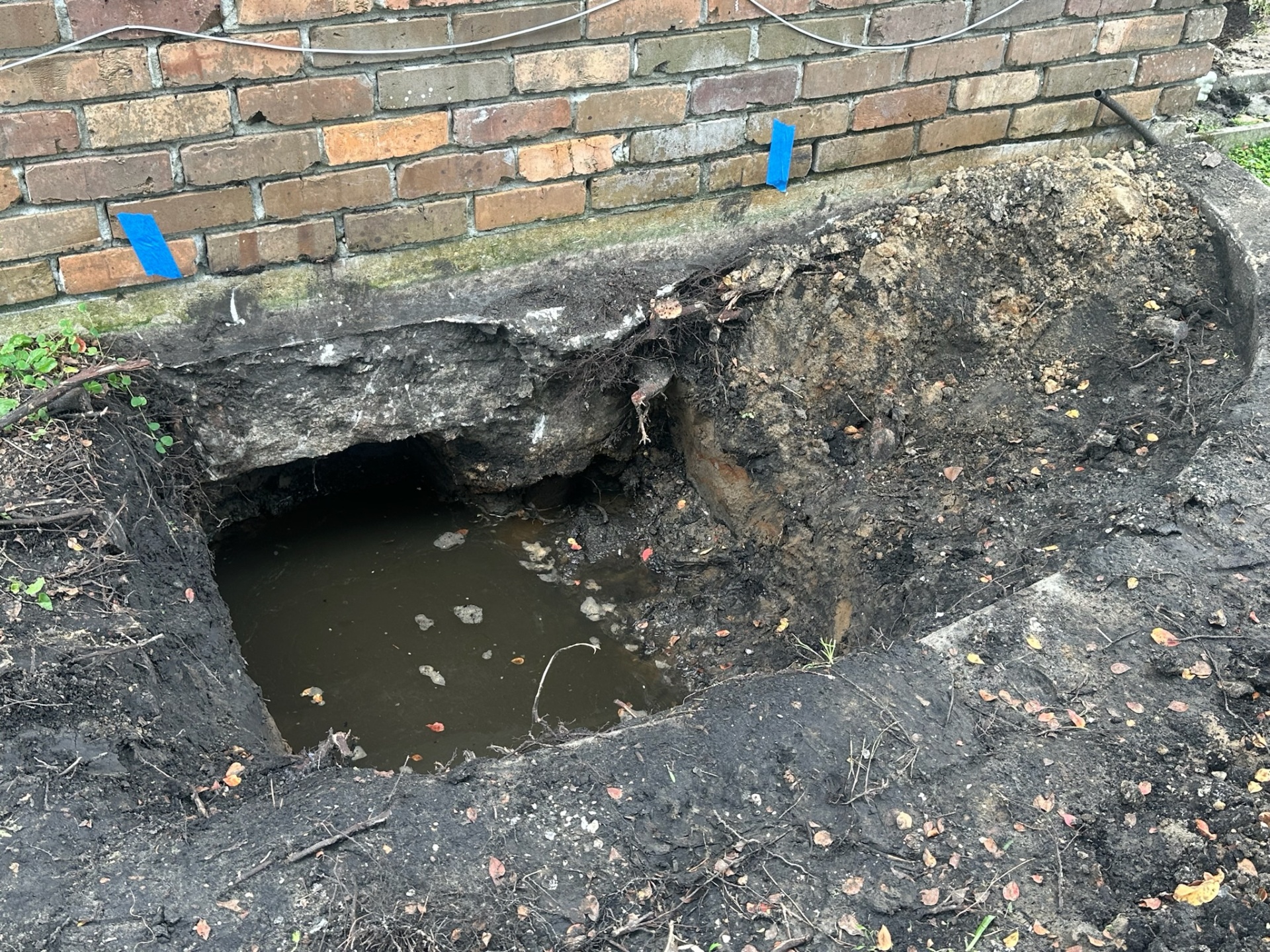 Excavation at the base of the original brick first floor in Metairie showing a hollowed-out area under the existing concrete and standing water where new foundation work was required to safely carry the added second-floor load