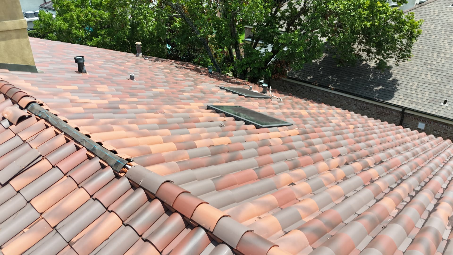 Aerial view of a terra cotta barrel tile roof with skylights and a ridge run with loose flashing in Metairie Louisiana