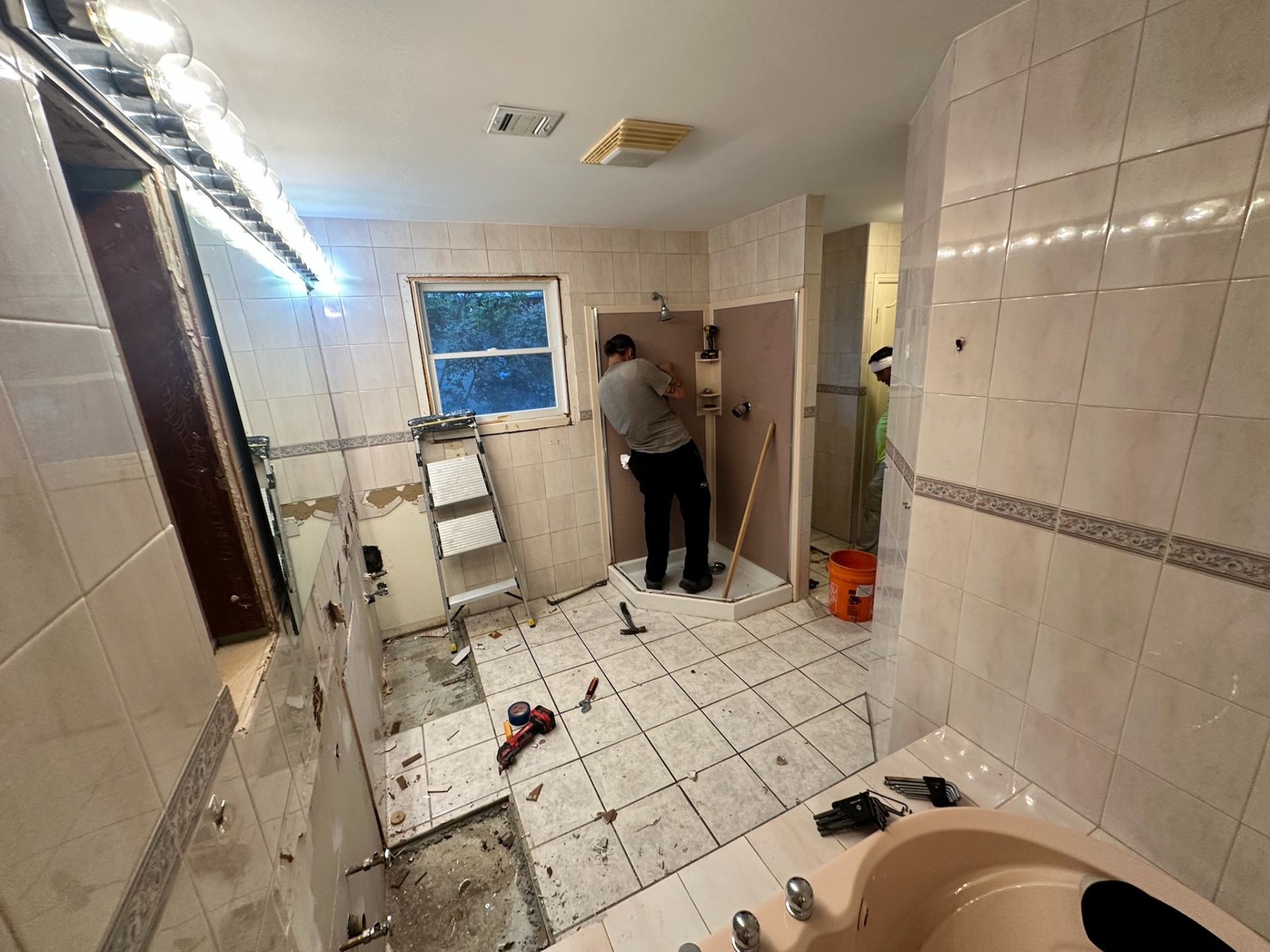 Old neo-angle shower stall and peach jetted tub during Metairie master bath demo in progress