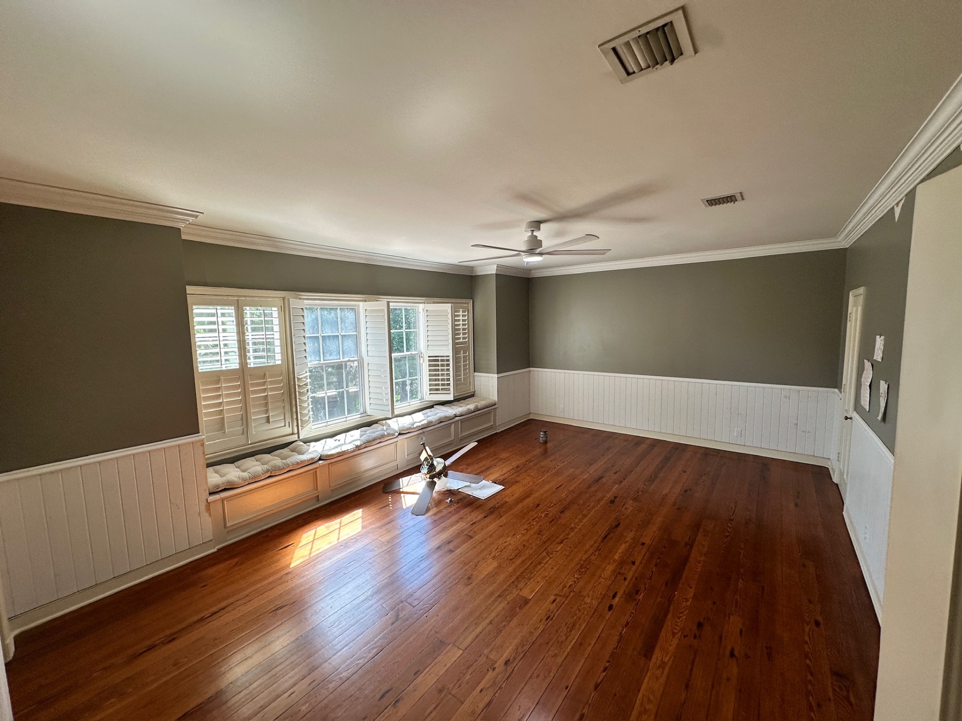 Finished beadboard wainscoting wrapping the bay window and built-in window seat cushions in a Covington LA bedroom with sage green walls and heart pine floors