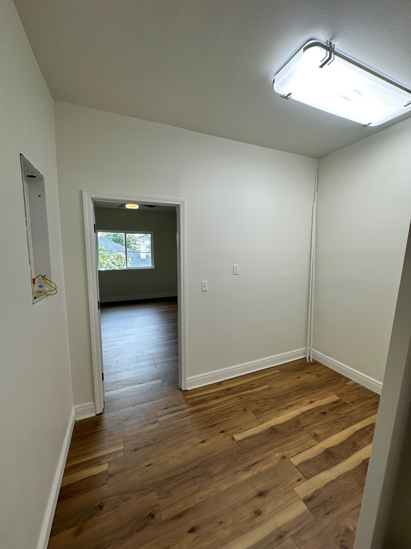 Finished second-floor laundry / utility closet on the Metairie addition with LED ceiling light, wide-plank LVP flooring, recessed panel rough-in on the wall and open doorway into the new bedroom beyond