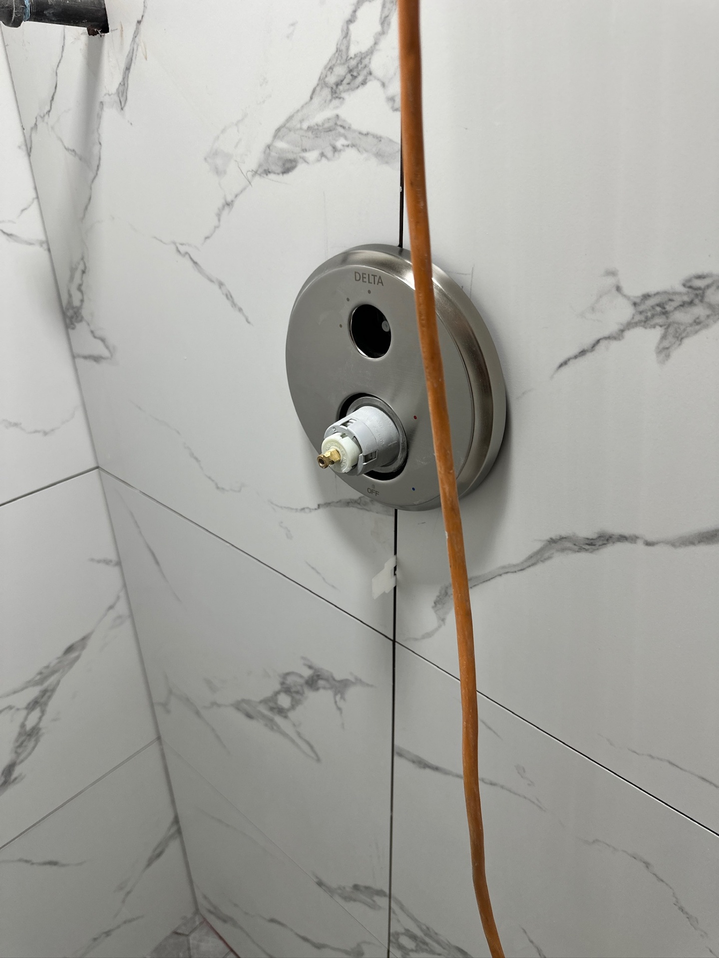 Close-up of Delta brushed nickel round shower valve trim on marble-look porcelain in Metairie master bath