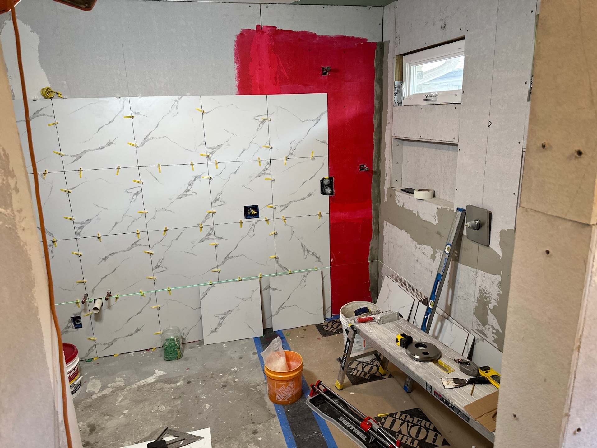Wide view of Metairie master bath shower mid-tile with marble-look porcelain, exposed niches, and shower valve trim ready