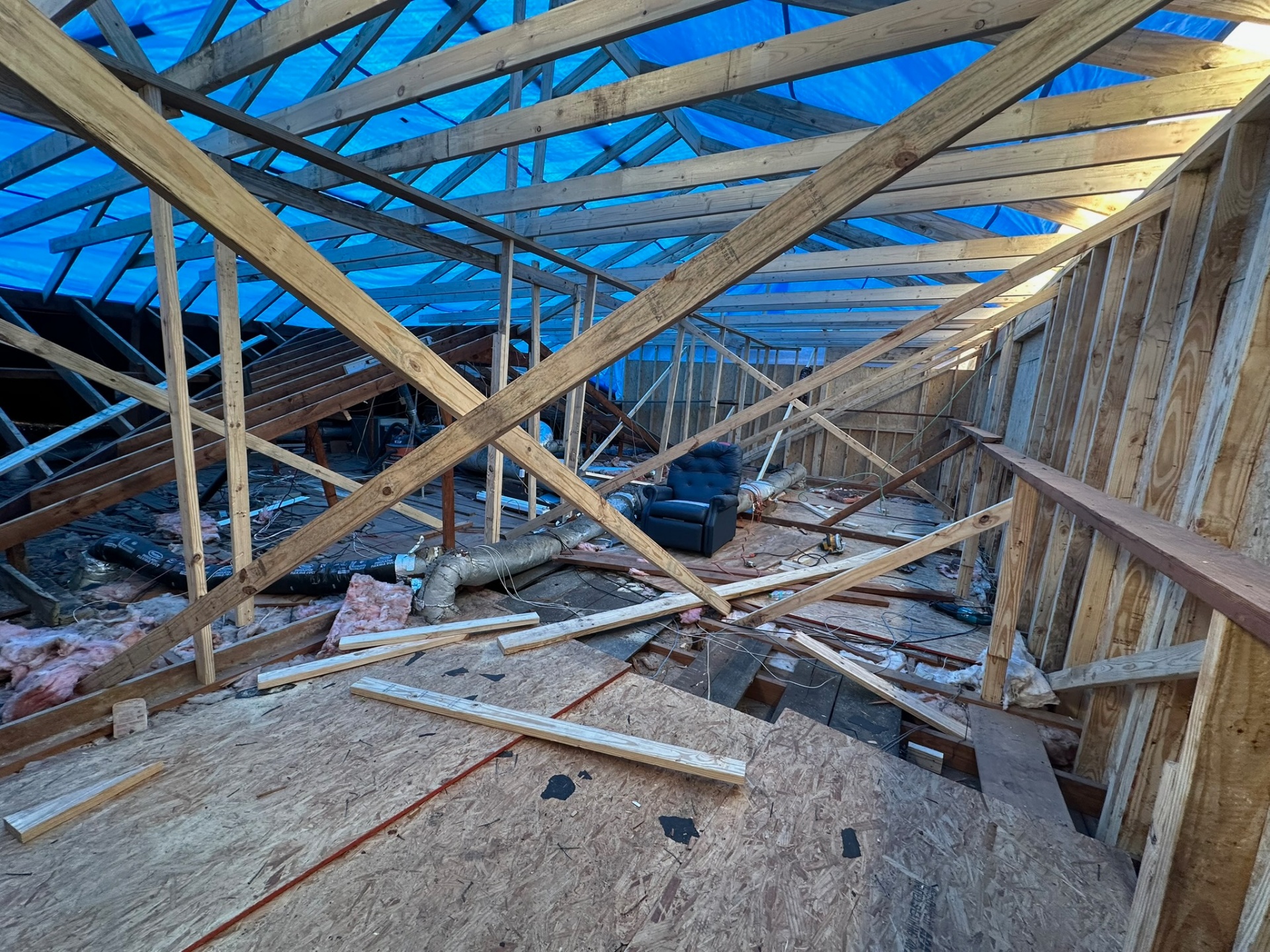 Wide interior view of Metairie attic with new rafters bracing and blue tarp suspended overhead protecting the home during second-floor addition
