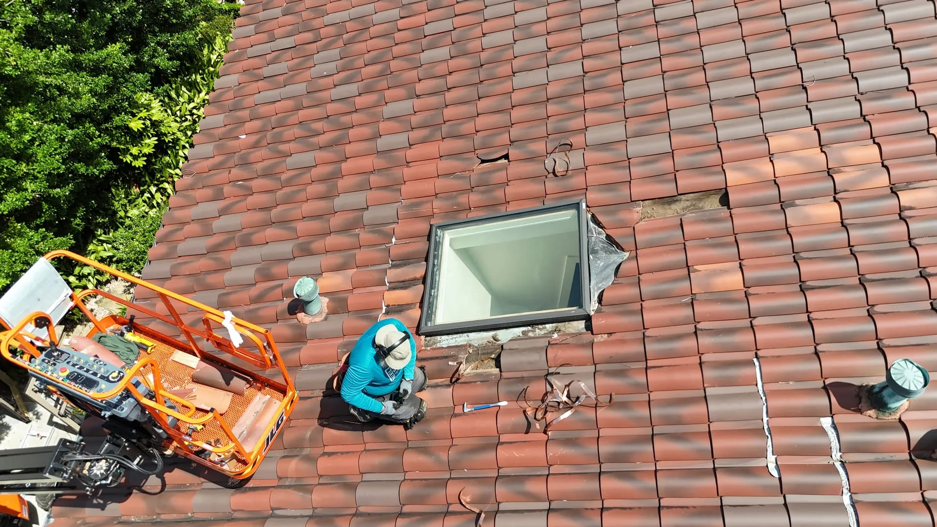Aerial view of Cajun Home Services roofer removing broken terra cotta tiles around a skylight from a boom lift in Metairie Louisiana