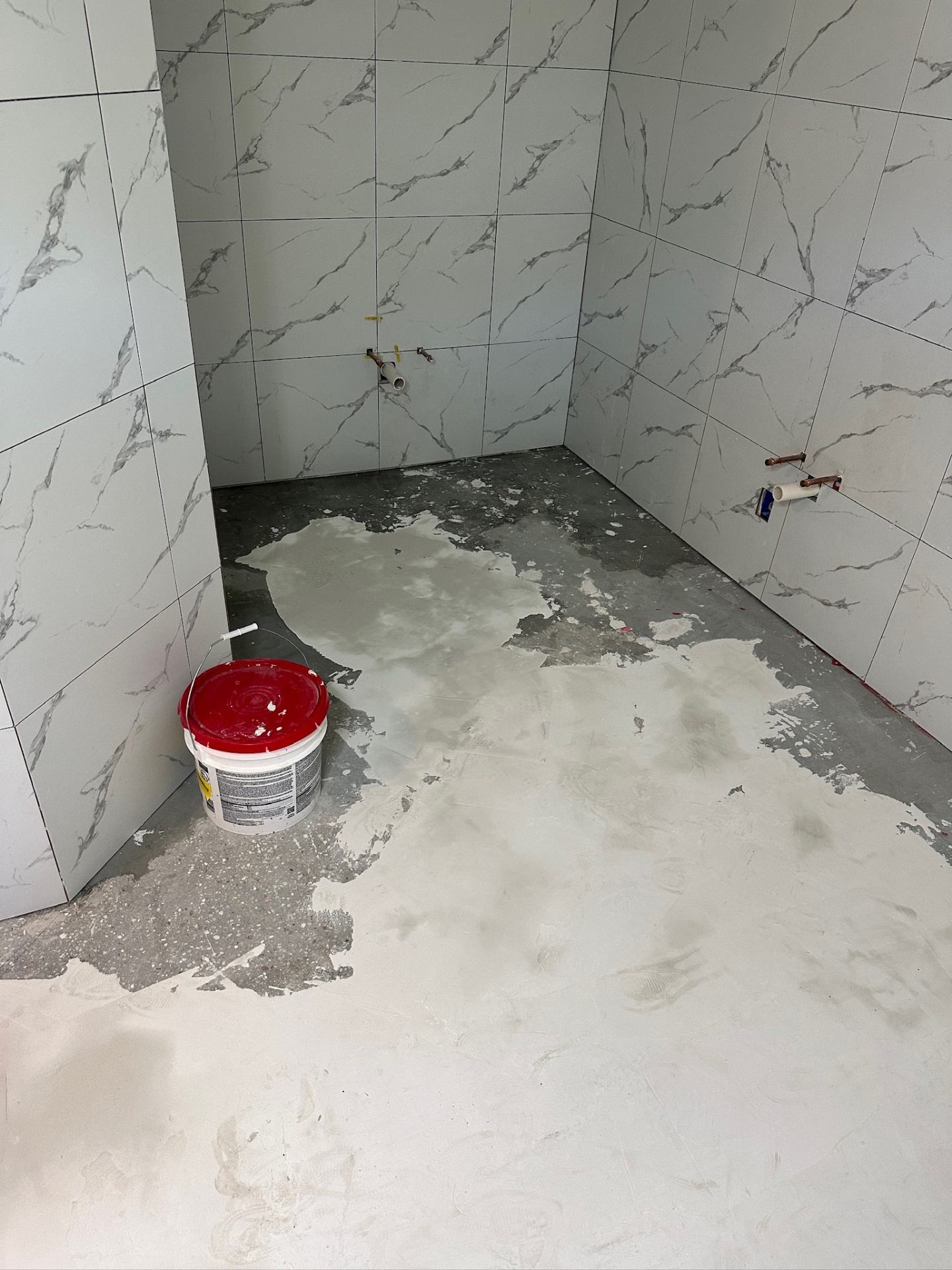 Water closet alcove floor prepped with self-leveling compound around new supply and drain stubs in Metairie master bath