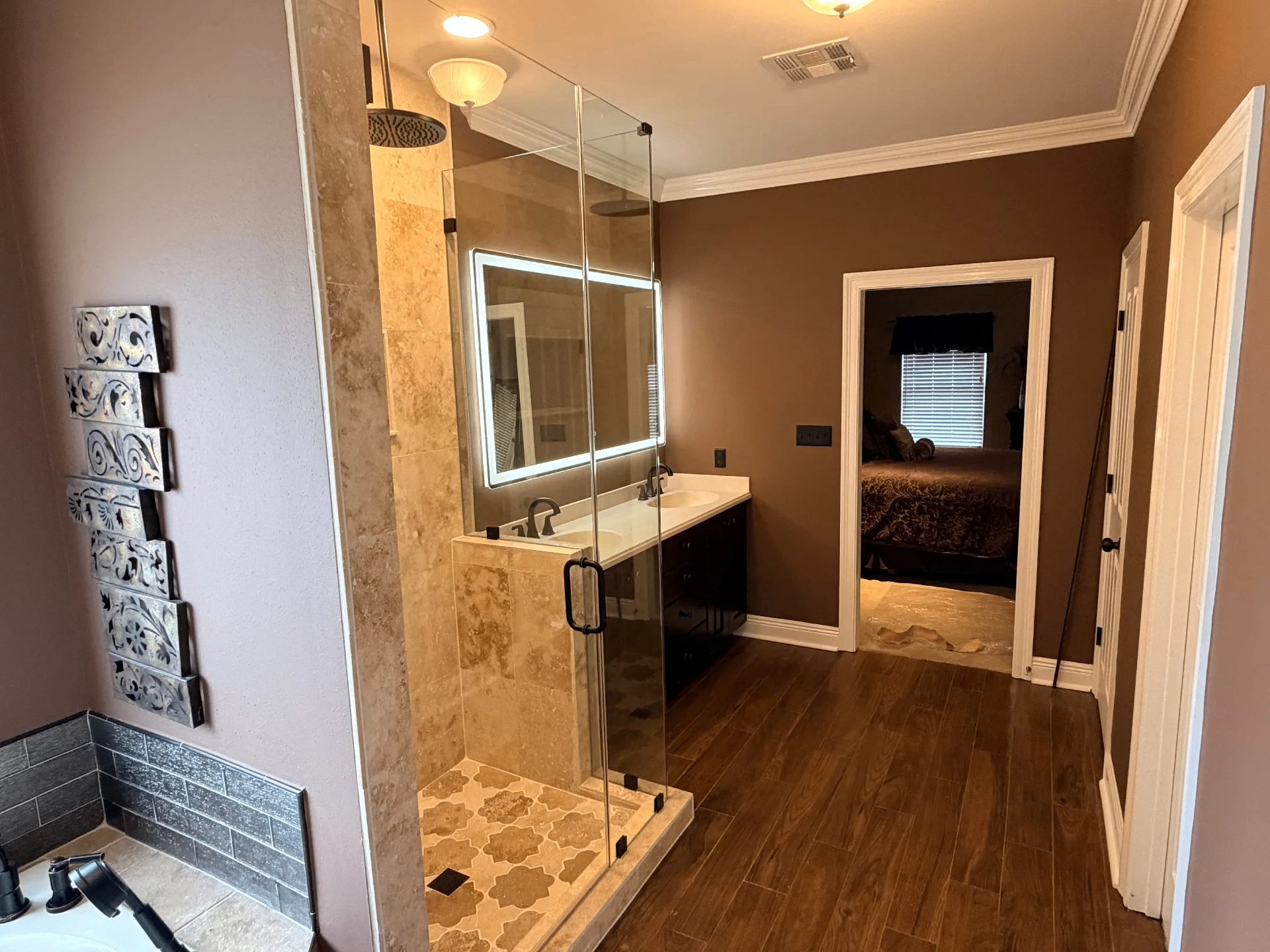 Completed master bathroom remodel in Destrehan Louisiana with travertine tile shower, rain heads, frameless glass enclosure, LED backlit mirror, and dark vanity by Cajun Home Services
