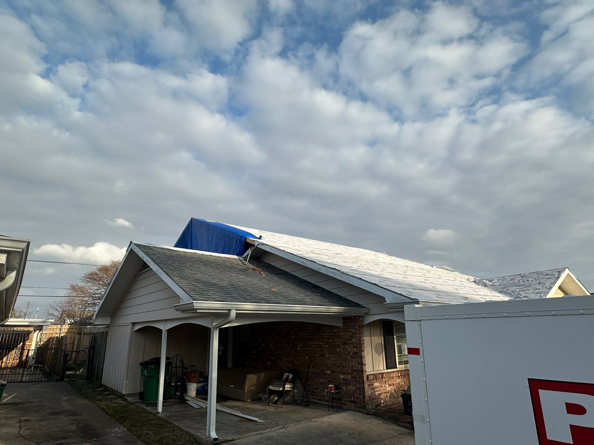 Side view of original Metairie home with existing shingle roof and blue tarp protecting the area where second-floor tear-off is starting
