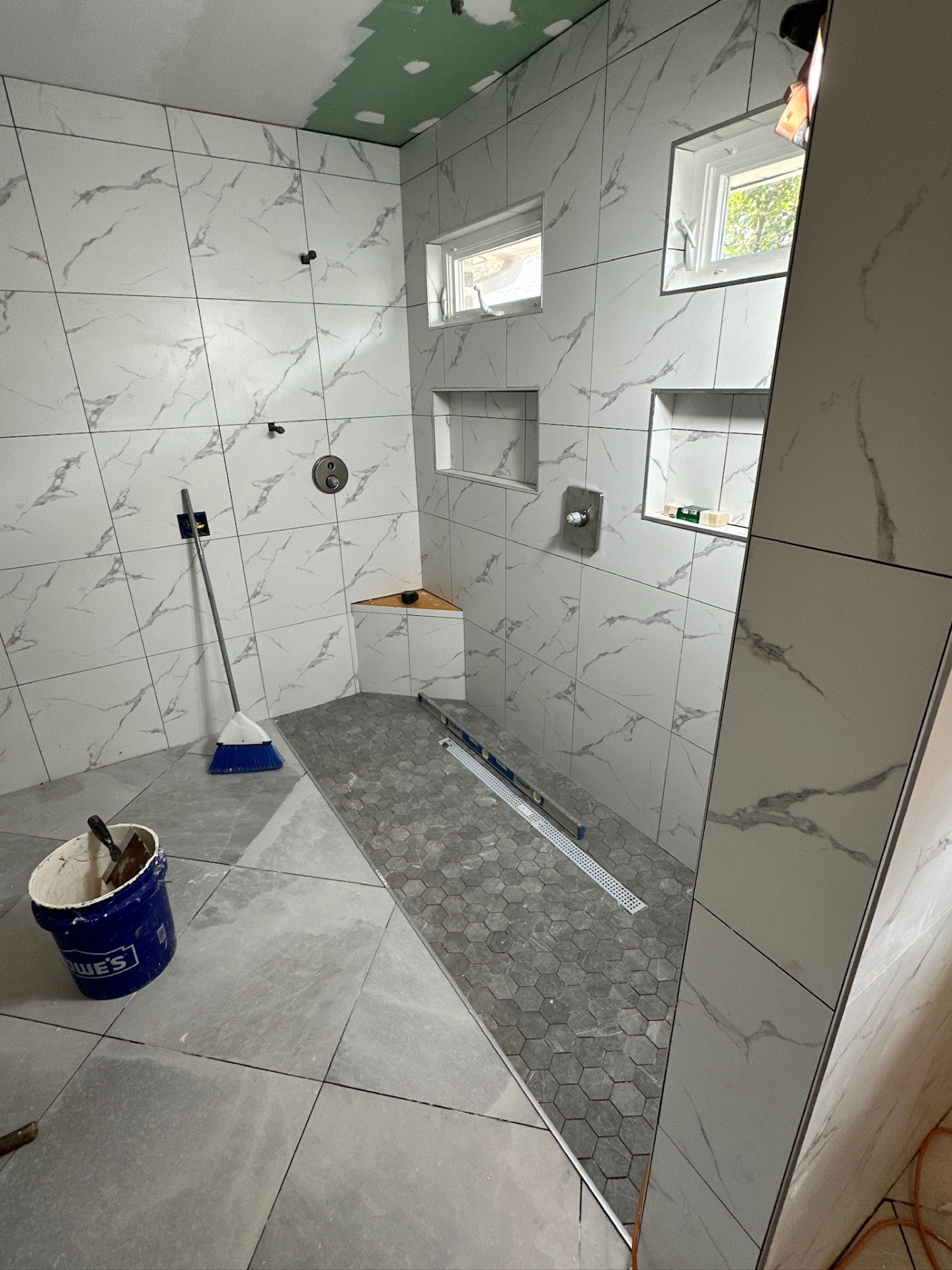 Linear drain checked for slope across gray hex mosaic shower floor in Metairie master bath