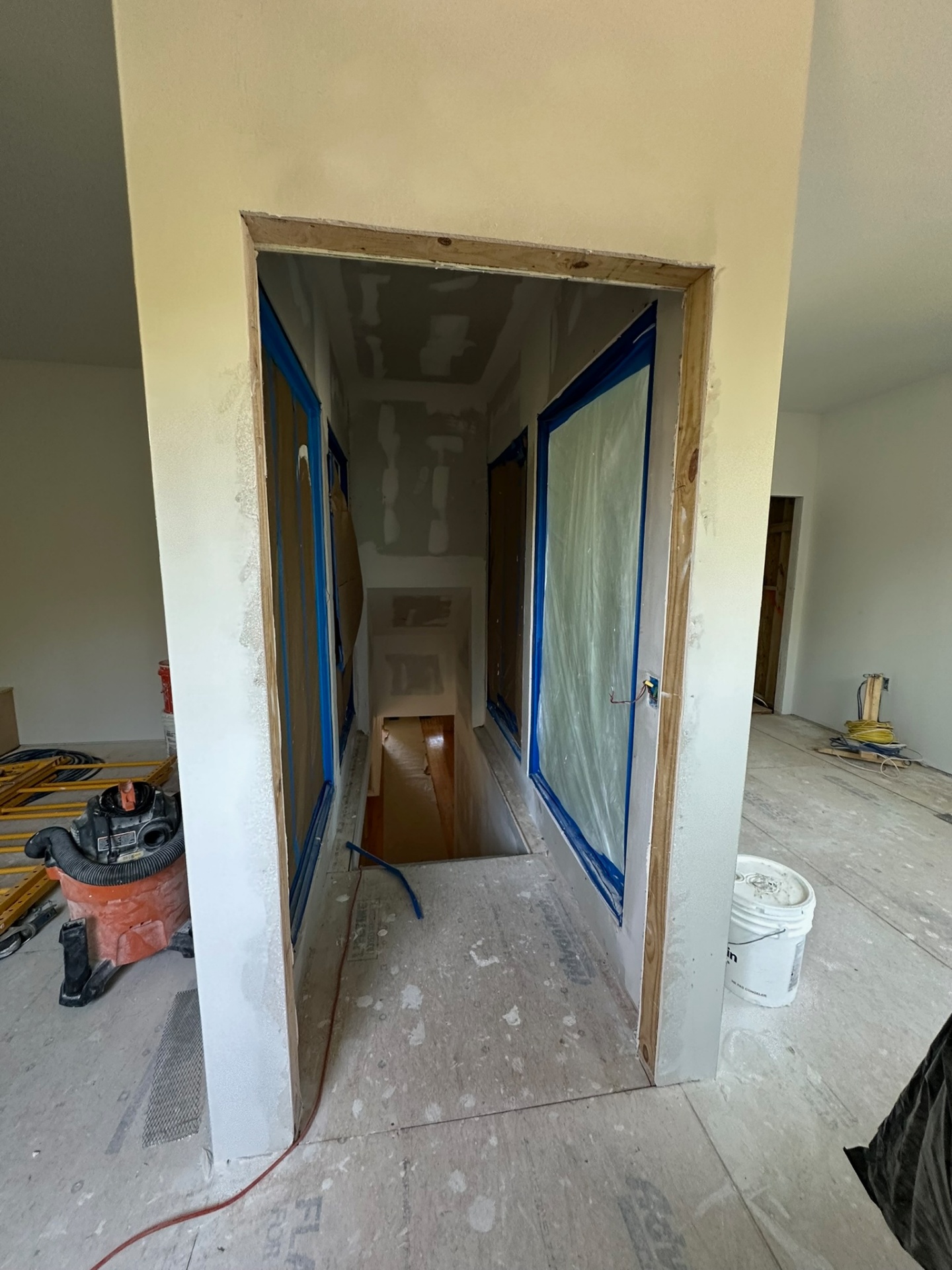 New stairwell opening on the second floor of the Metairie addition with drywall hung and seams taped, blue painters tape masking the rough opening for a future glass railing system