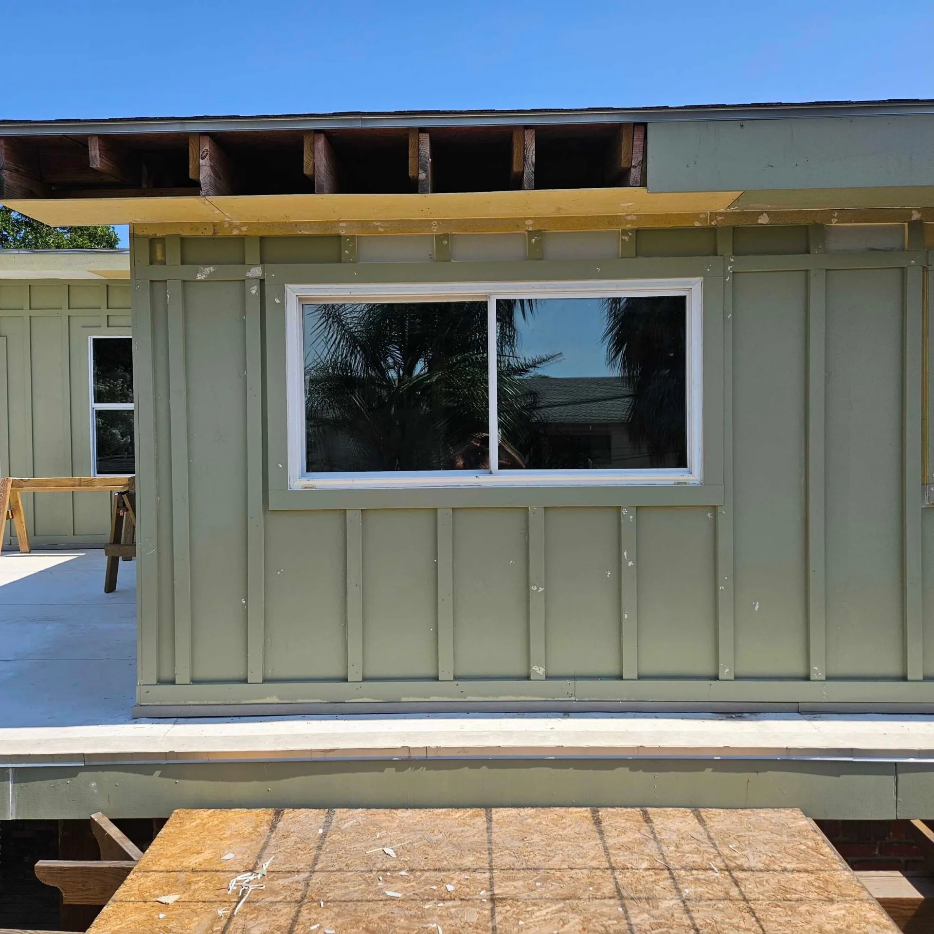 Rear elevation detail at Blanke Street Metairie home with finished green board-and-batten siding, white trim, and a new white slider window