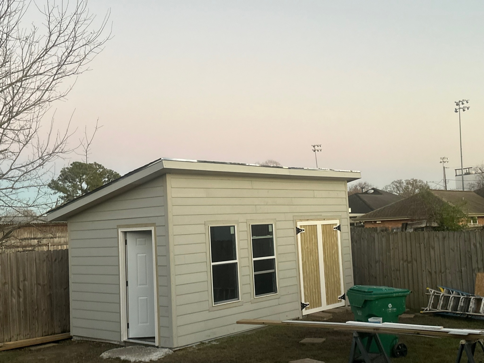 Dusk shot of Metairie outbuilding in primer with side entry door open, raw barn doors hung, ready for final paint