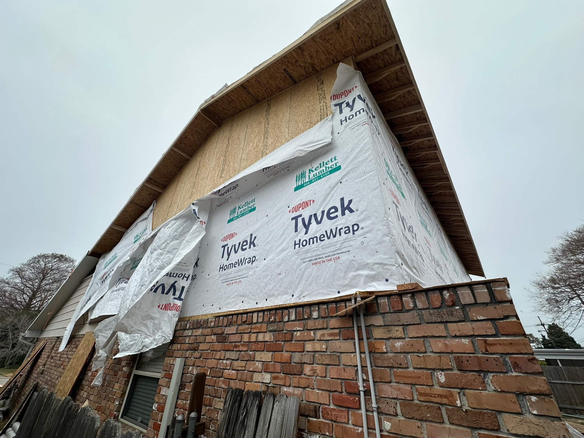 Front gable corner of Metairie second-floor addition wrapped in Tyvek with sheathing and gable end visible above the original brick first floor
