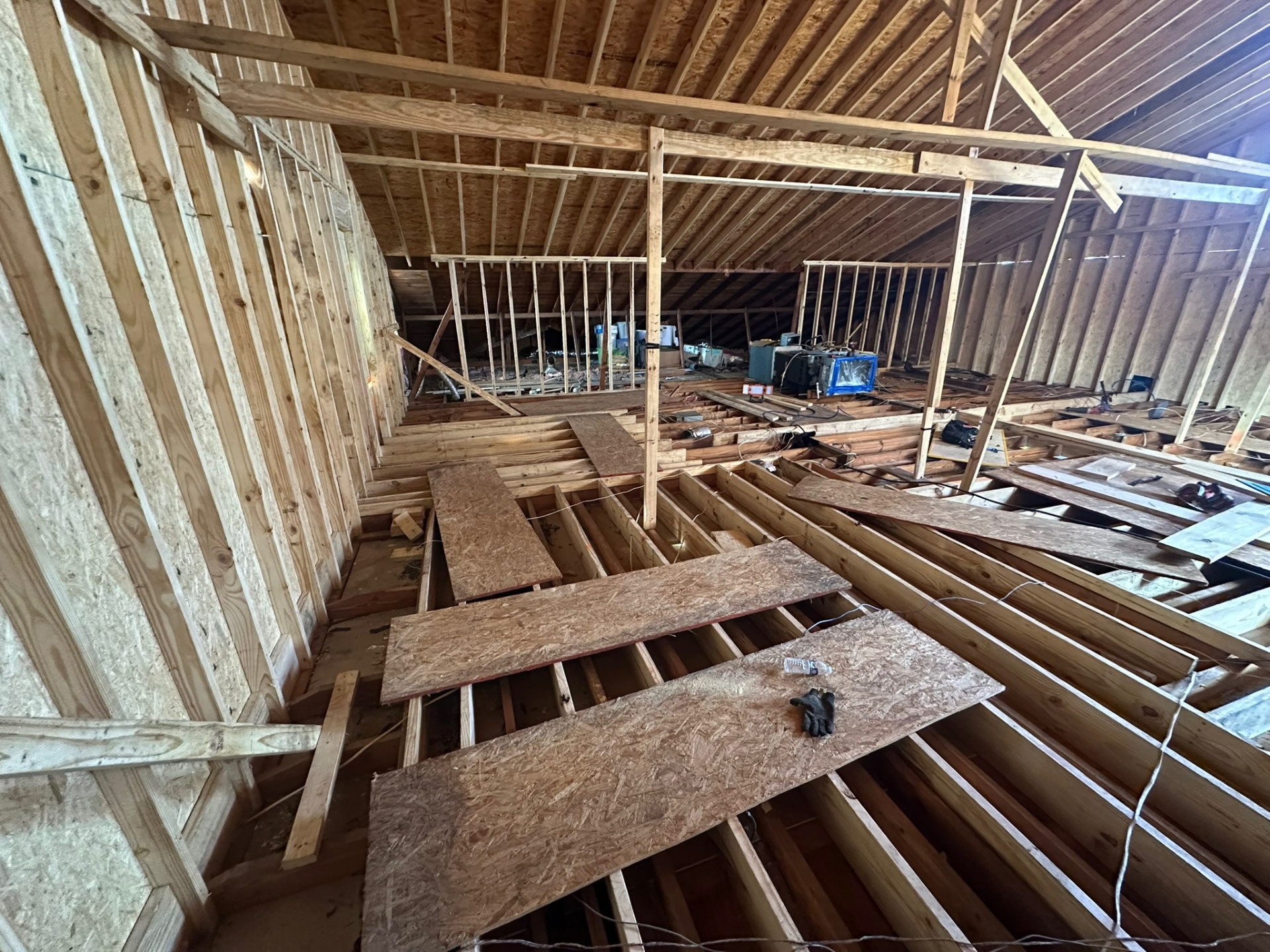 Interior of Metairie second-floor framing with knee walls and OSB-sheathed perimeter walls in place under new rafters, exposed floor joists visible across the open span