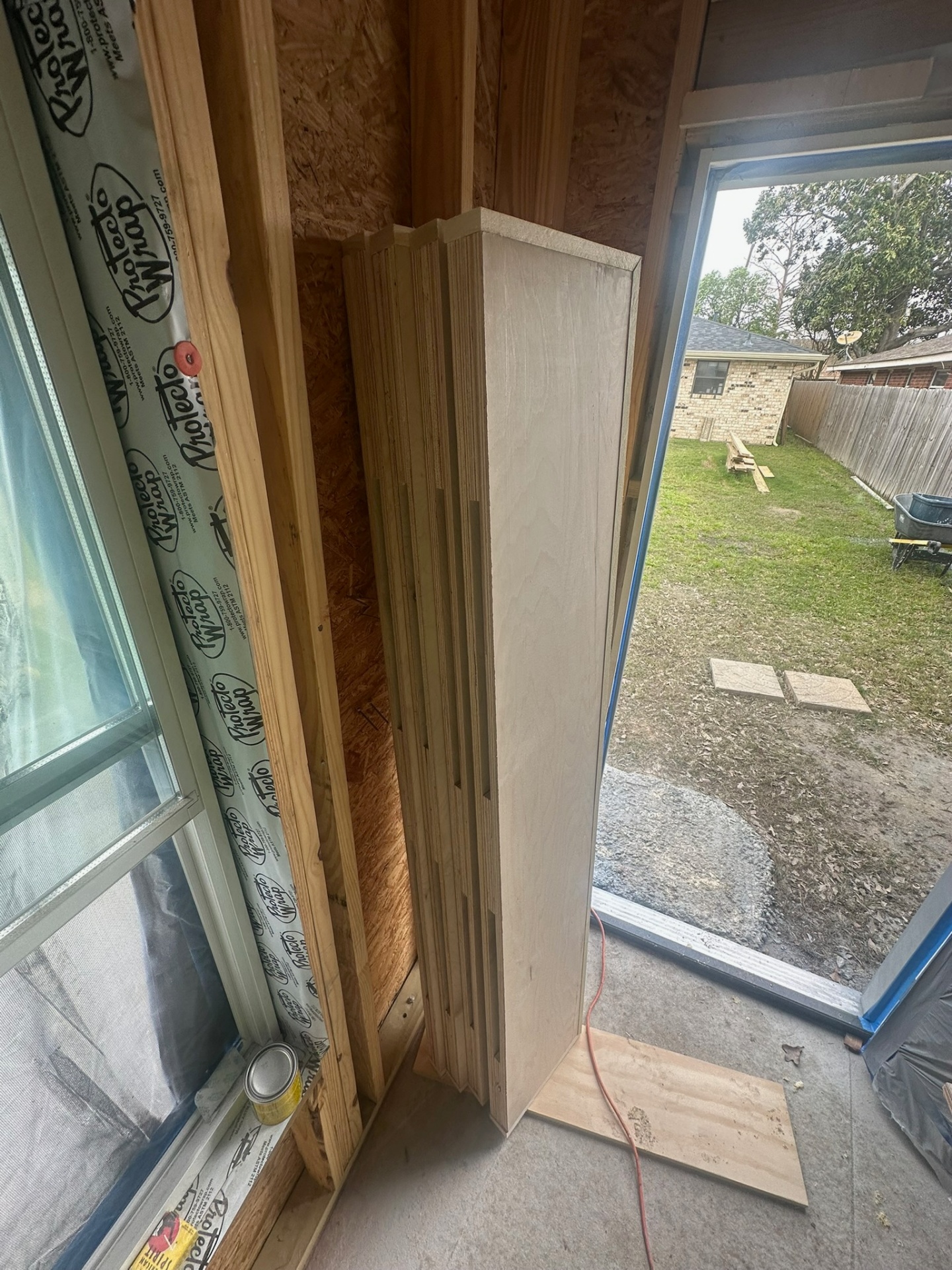 Stack of raw unfinished maple floating shelves staged inside the Meraux LA home next to a window opening and Protecto Wrap flashing before staining and install