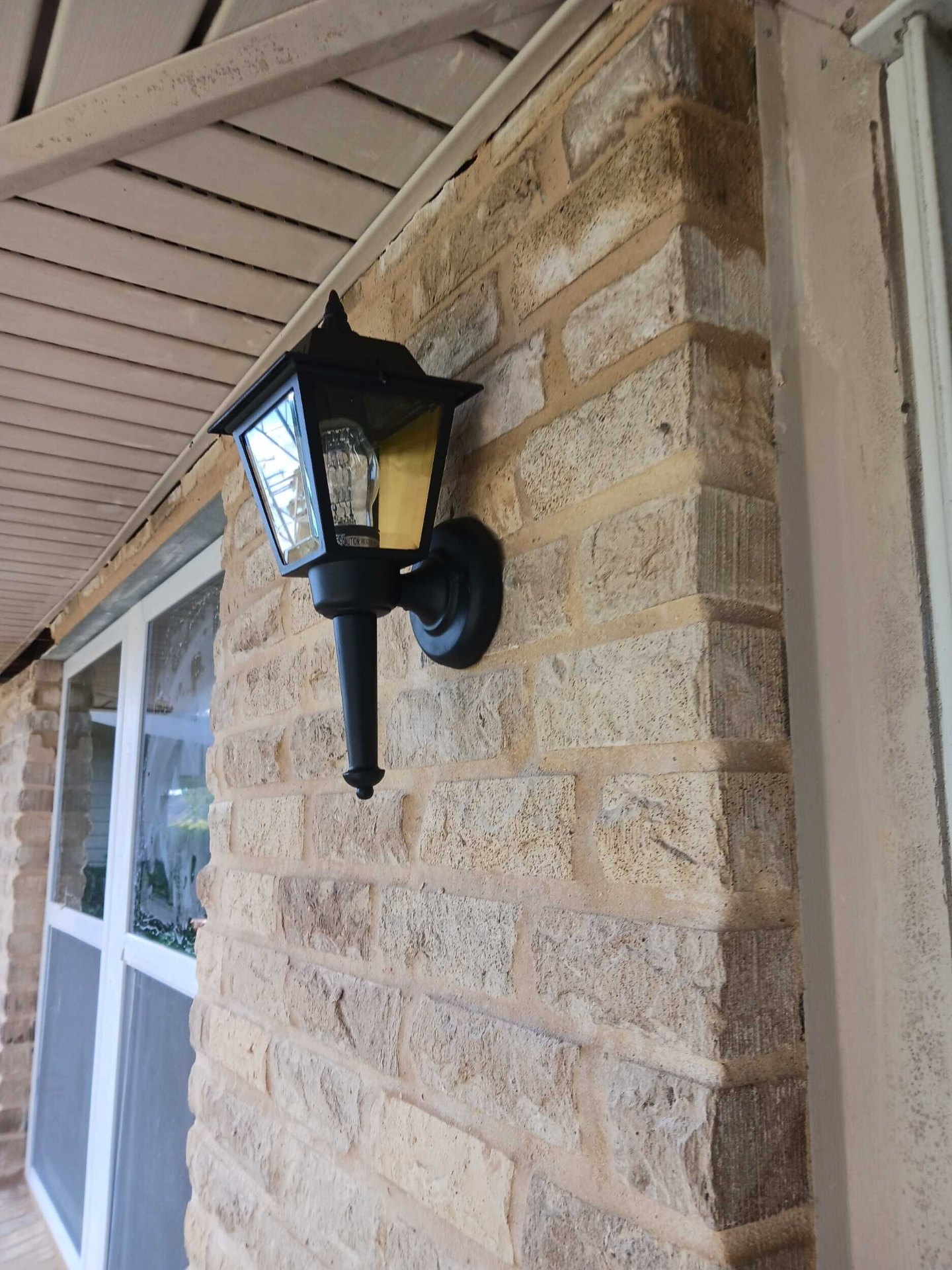 New black exterior lantern-style wall light reinstalled on the rebuilt brick veneer at the Gretna front porch