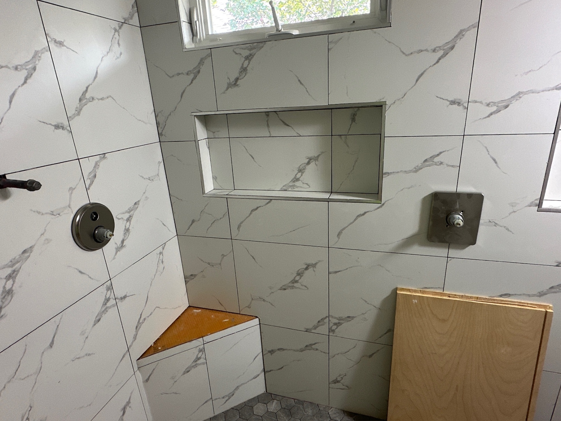 Shower niche, corner bench dry-fit, and Delta valve stubs on marble-look porcelain in Metairie master bath