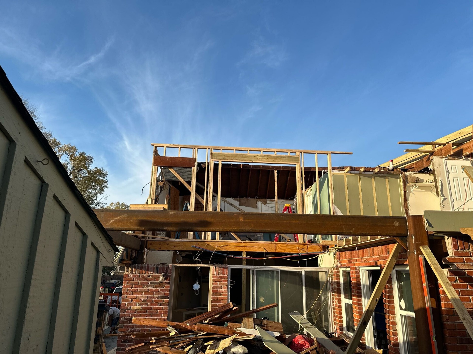 Rear elevation of Blanke Street Metairie home mid-demo with original brick first floor exposed and second-story framing starting above