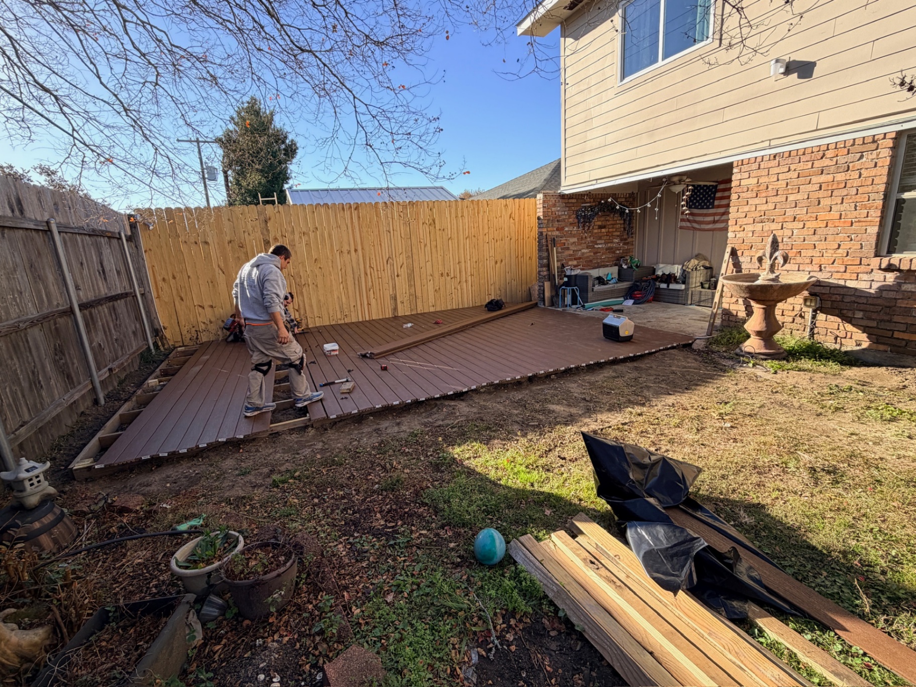 Cajun Home Services carpenter installing composite decking with brick chimney and back porch behind in Metairie Louisiana