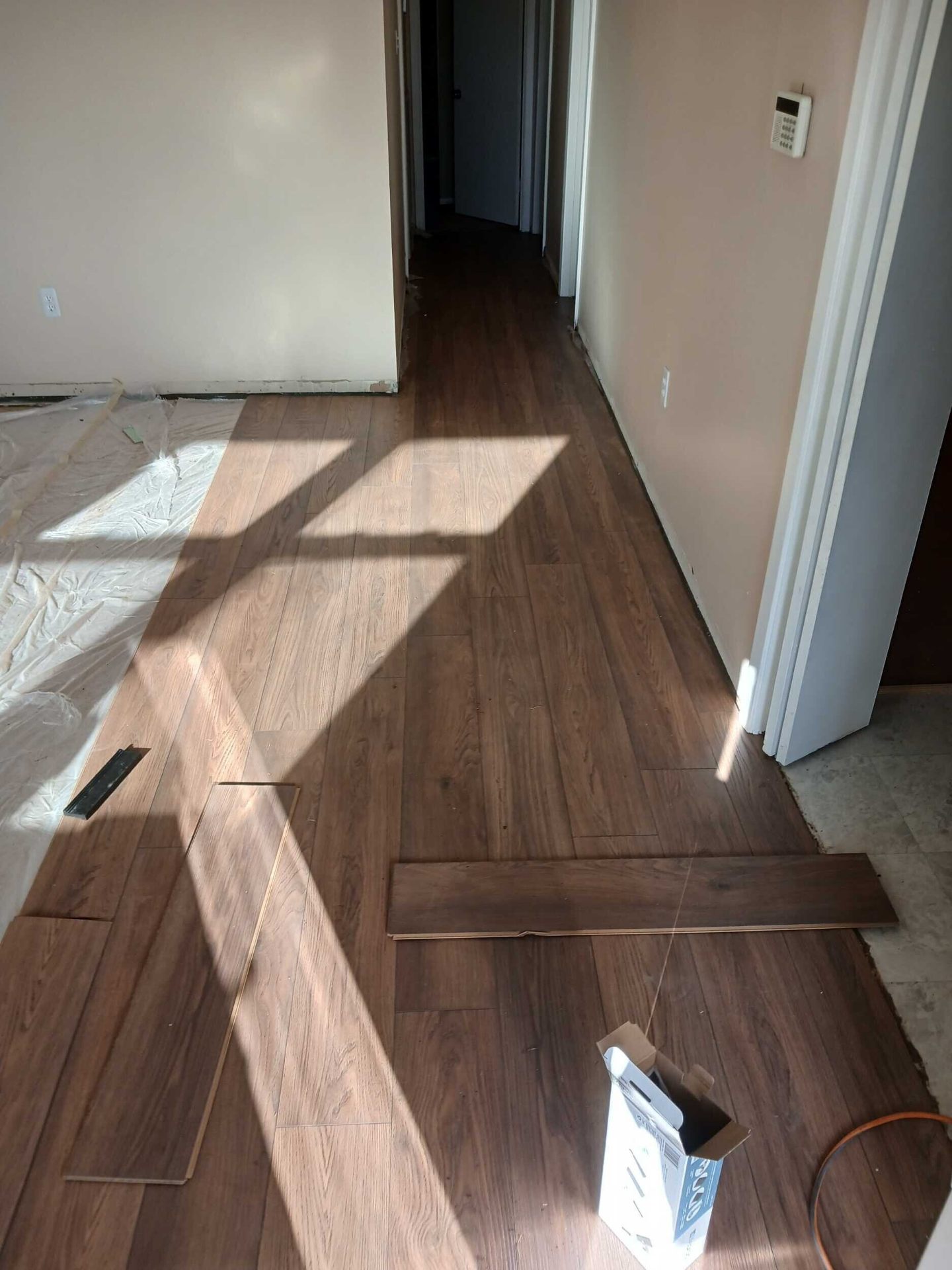 New wide-plank laminate flooring being installed through the Gretna hallway and living area with fresh planks staged for the next row