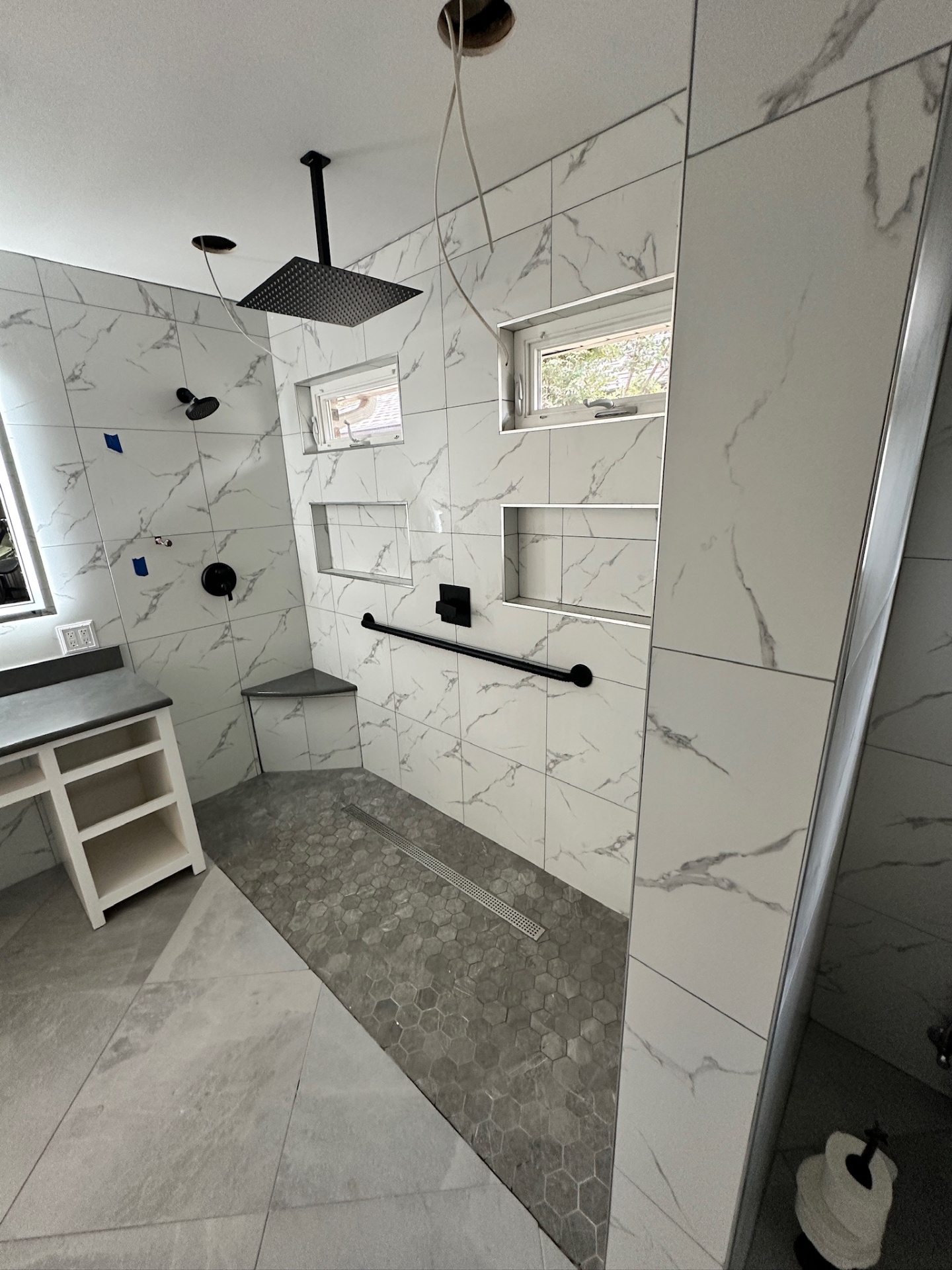 Walk-in shower with ceiling-mount rain head, hand shower, black grab bar, Delta valves, dual niches, and hex floor installed pre-grout in Metairie master bath