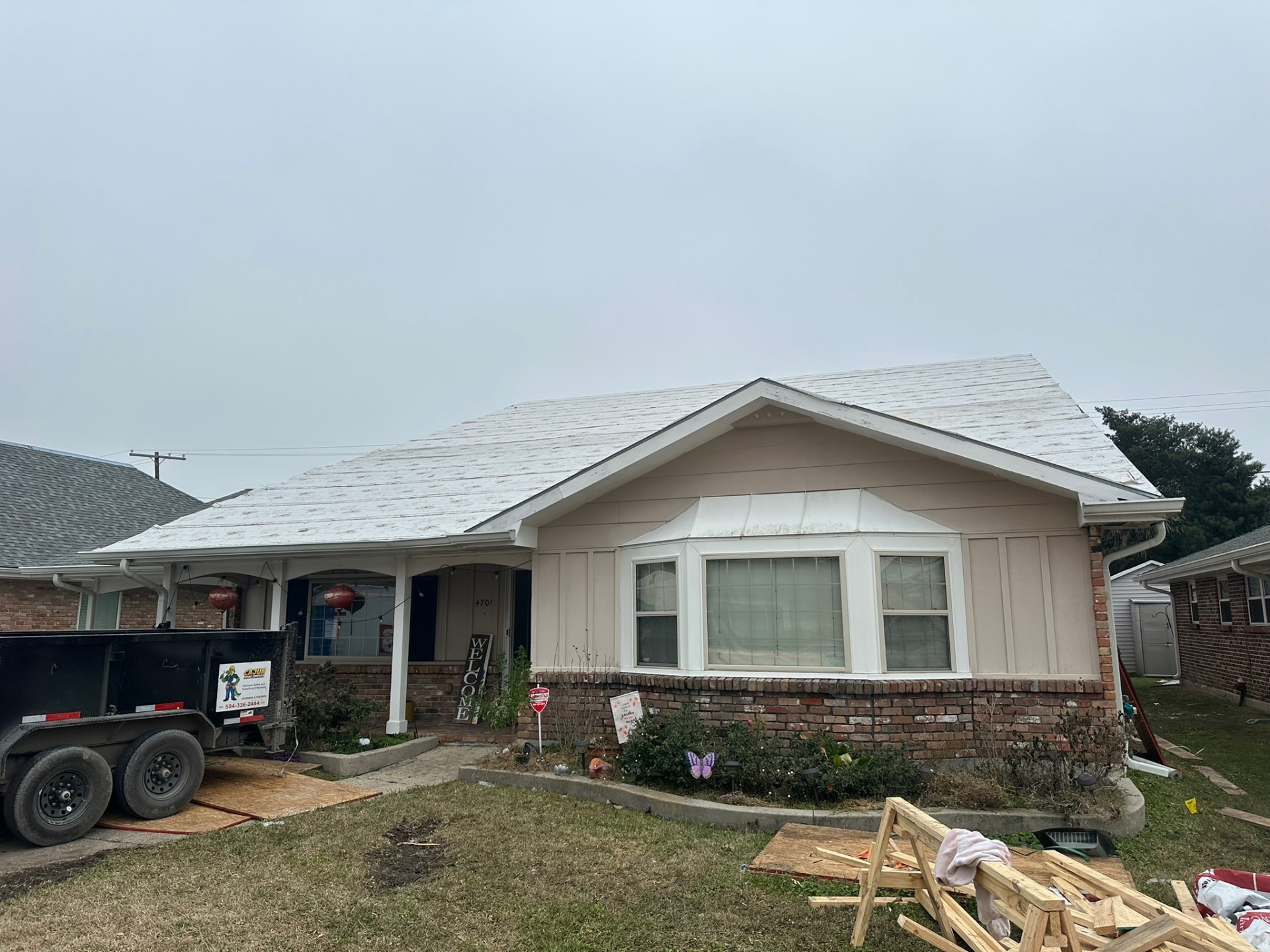 Front elevation of original single-story Metairie home with frost-covered shingle roof before second-floor addition tear-off, Cajun Home Services dump trailer staged at curb