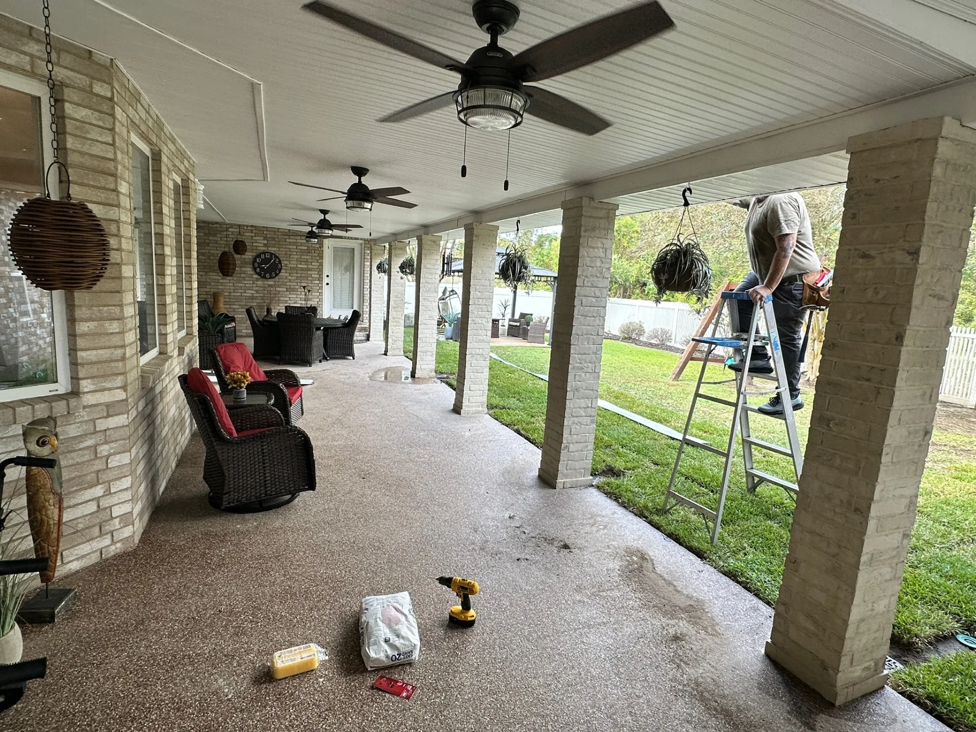 Cajun Home Services carpenter finishing ceiling fan and soffit trim under completed covered patio at Destrehan Louisiana home