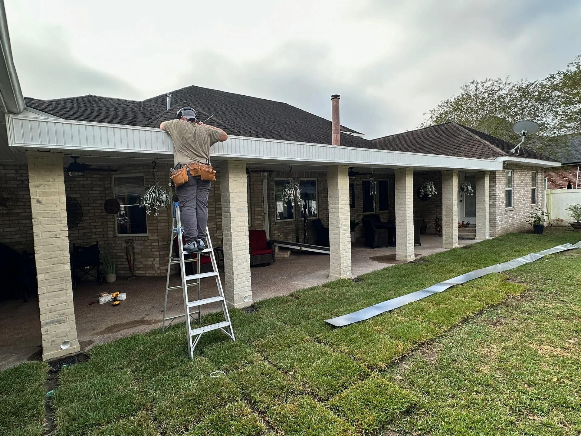 Cajun Home Services carpenter on ladder installing hidden gutter and fascia detail on rebuilt covered patio at Destrehan Louisiana home