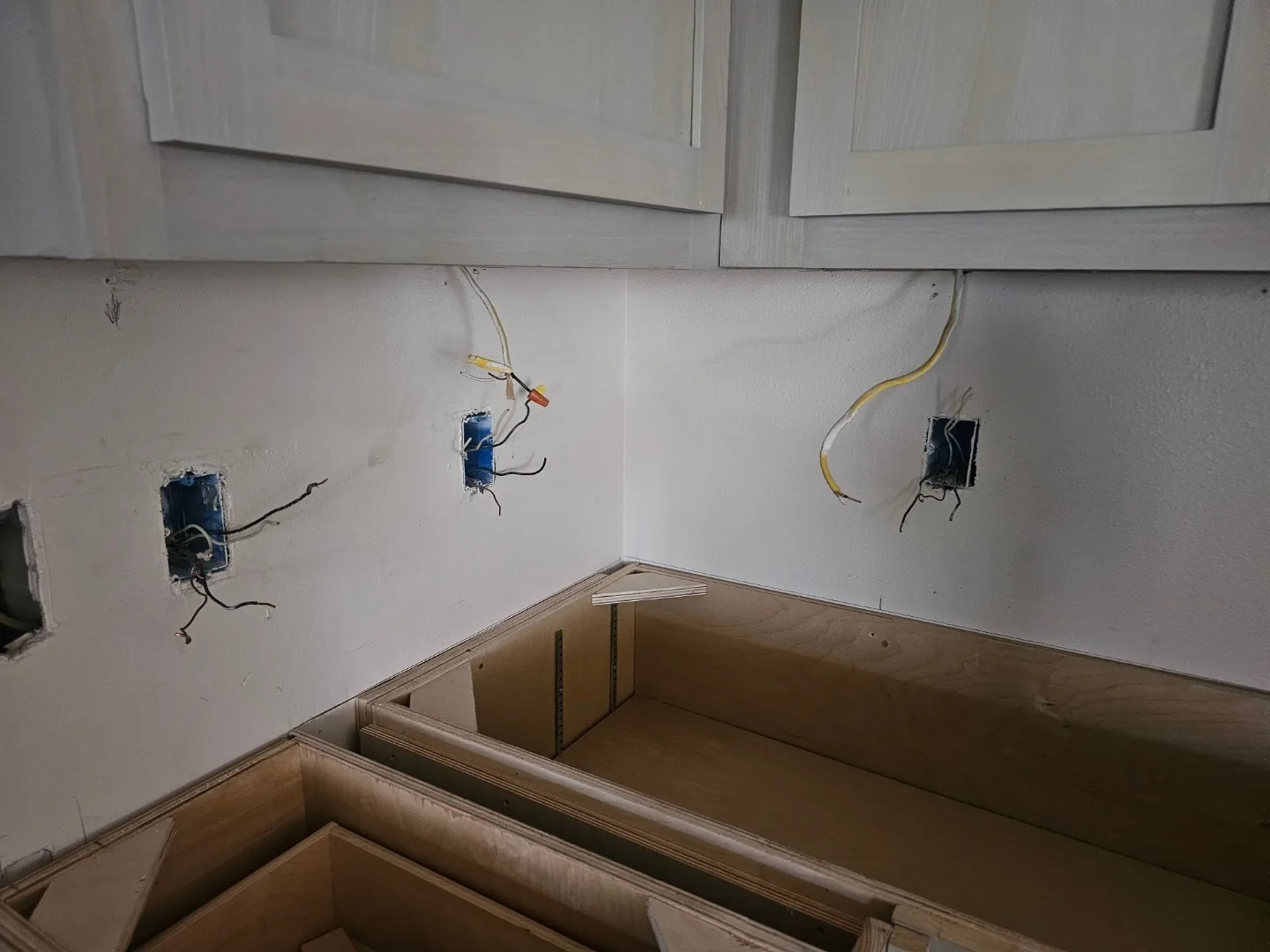 Kitchen electrical rough-in at Blanke Street Metairie home with new outlet boxes and wiring exposed above base cabinets before backsplash and countertops go in