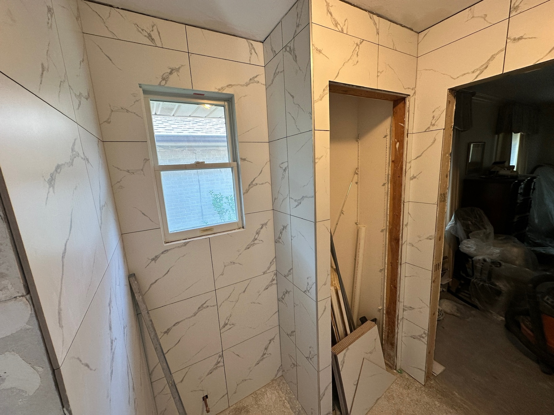 Bathroom entry with marble-look wall tile wrapping the window and doorway opening into the bedroom in Metairie master bath
