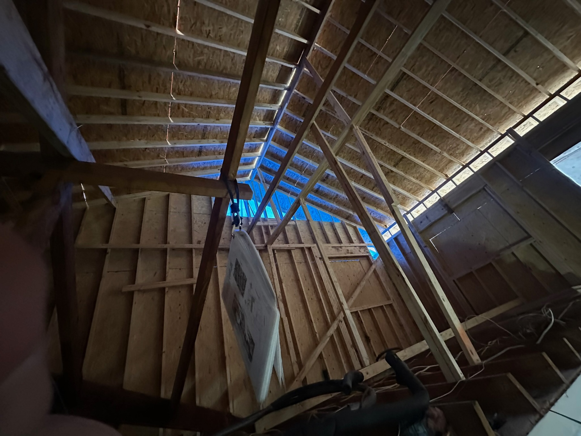 New roof rafters installed over Metairie second-floor addition with sky visible through partial decking and permit placard hung from beam