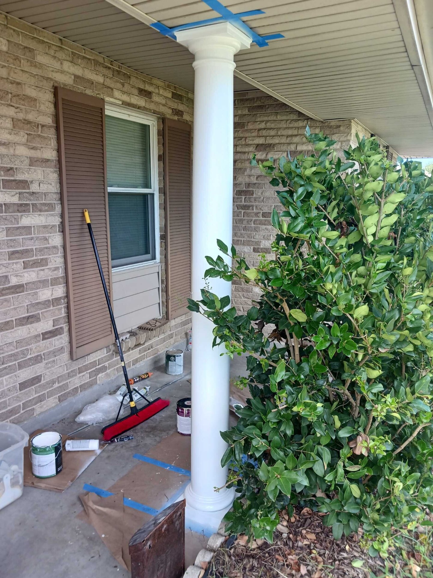 New white round porch column installed and painted on the Gretna front porch with paint supplies staged during exterior finish