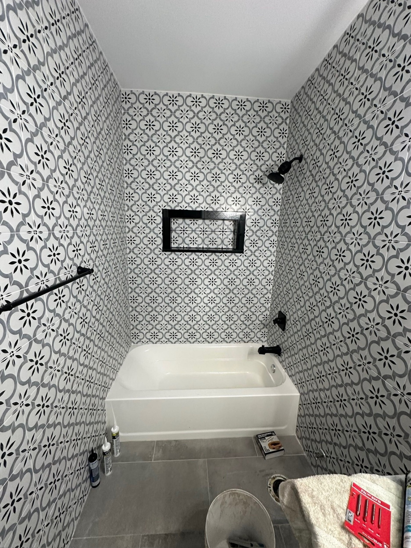 Interior view of finished tub surround in Meraux Louisiana bathroom with waterproofed recessed niche framed in black bullnose tile and floor to ceiling patterned porcelain