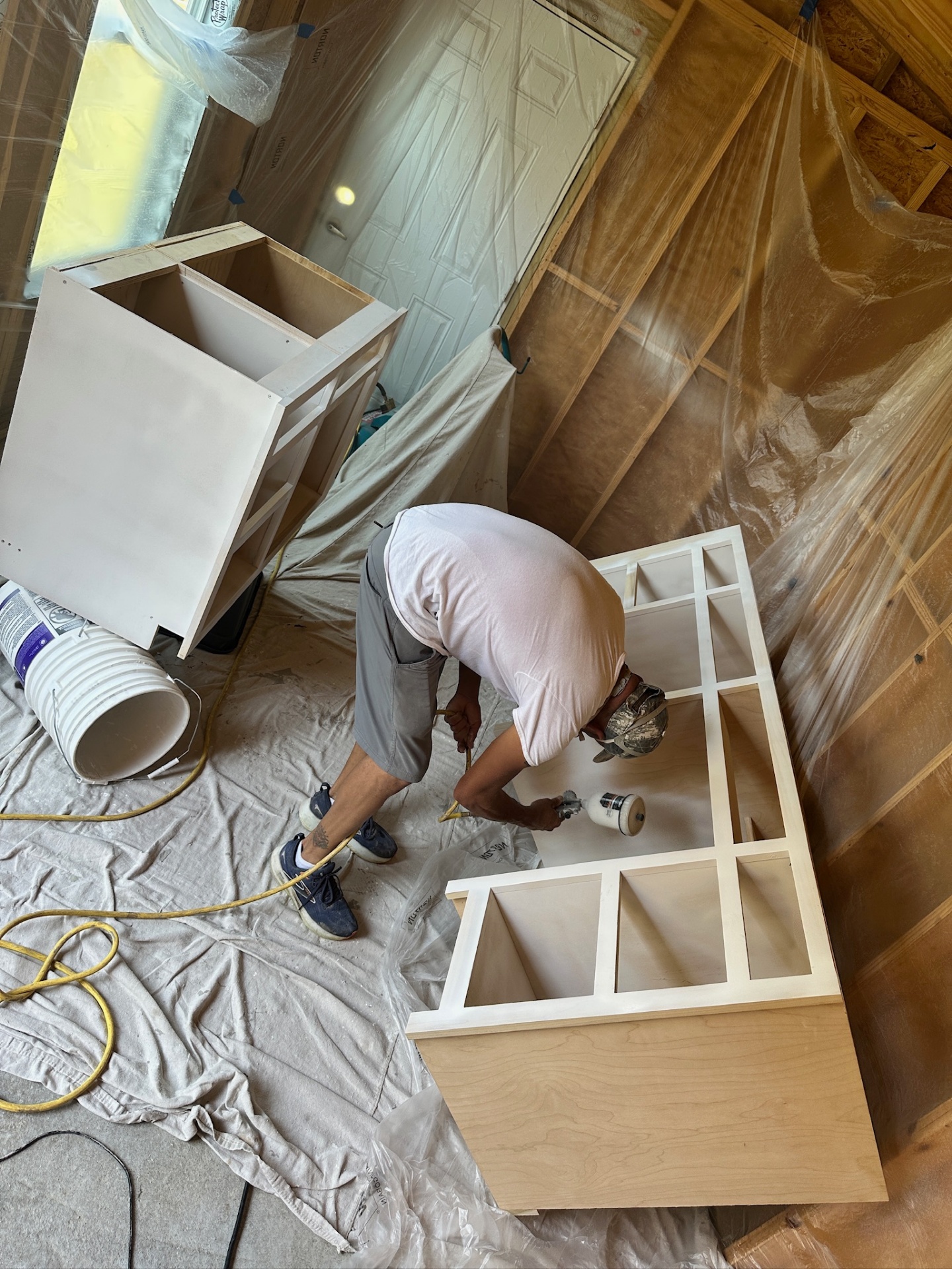 Cajun Home Services finisher spraying primer on custom vanity cabinet inside a plastic-tented shop at the Metairie master bath project
