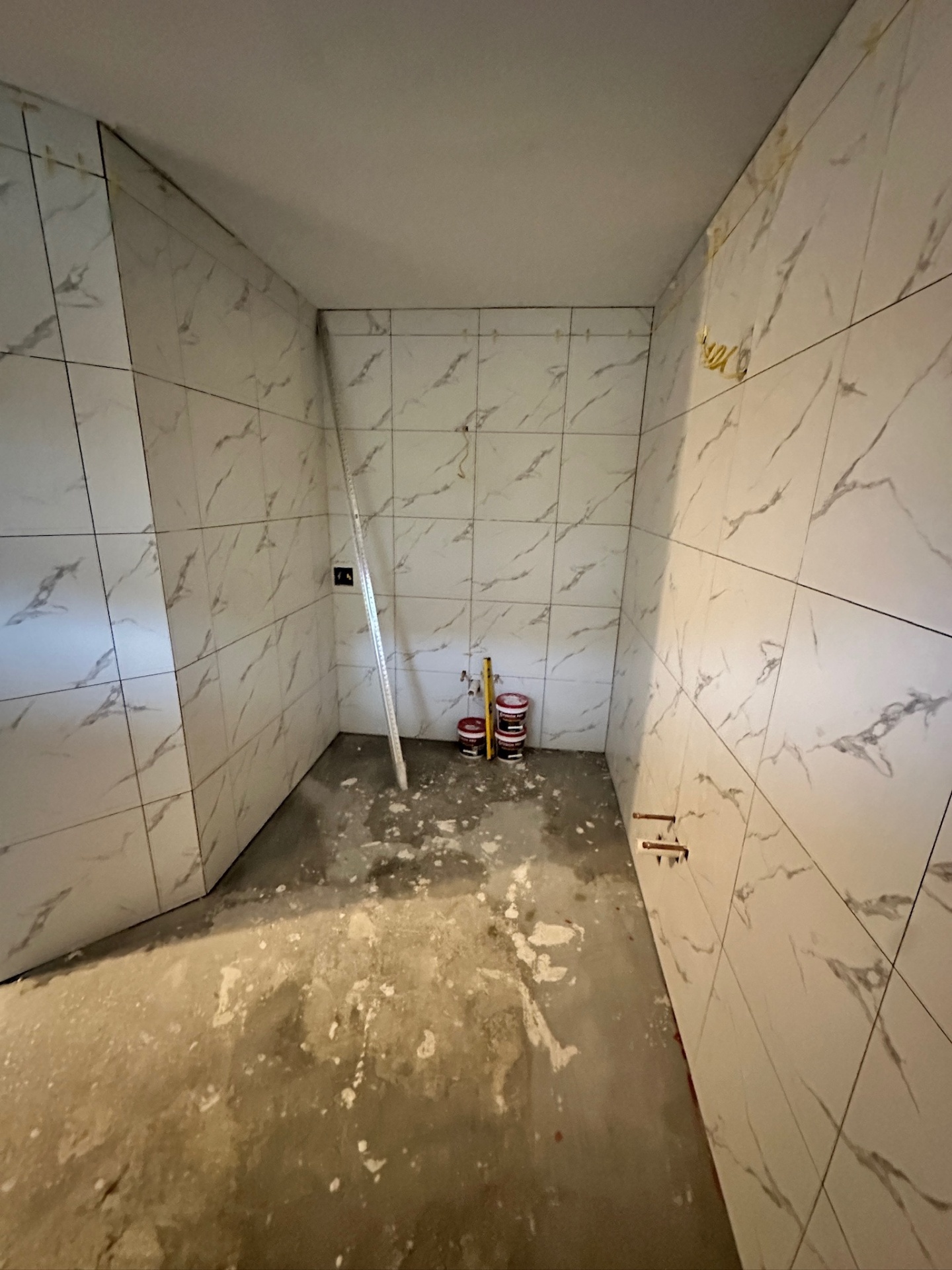 Water closet with marble-look wall tile complete and prepped concrete floor before hex tile in Metairie master bath