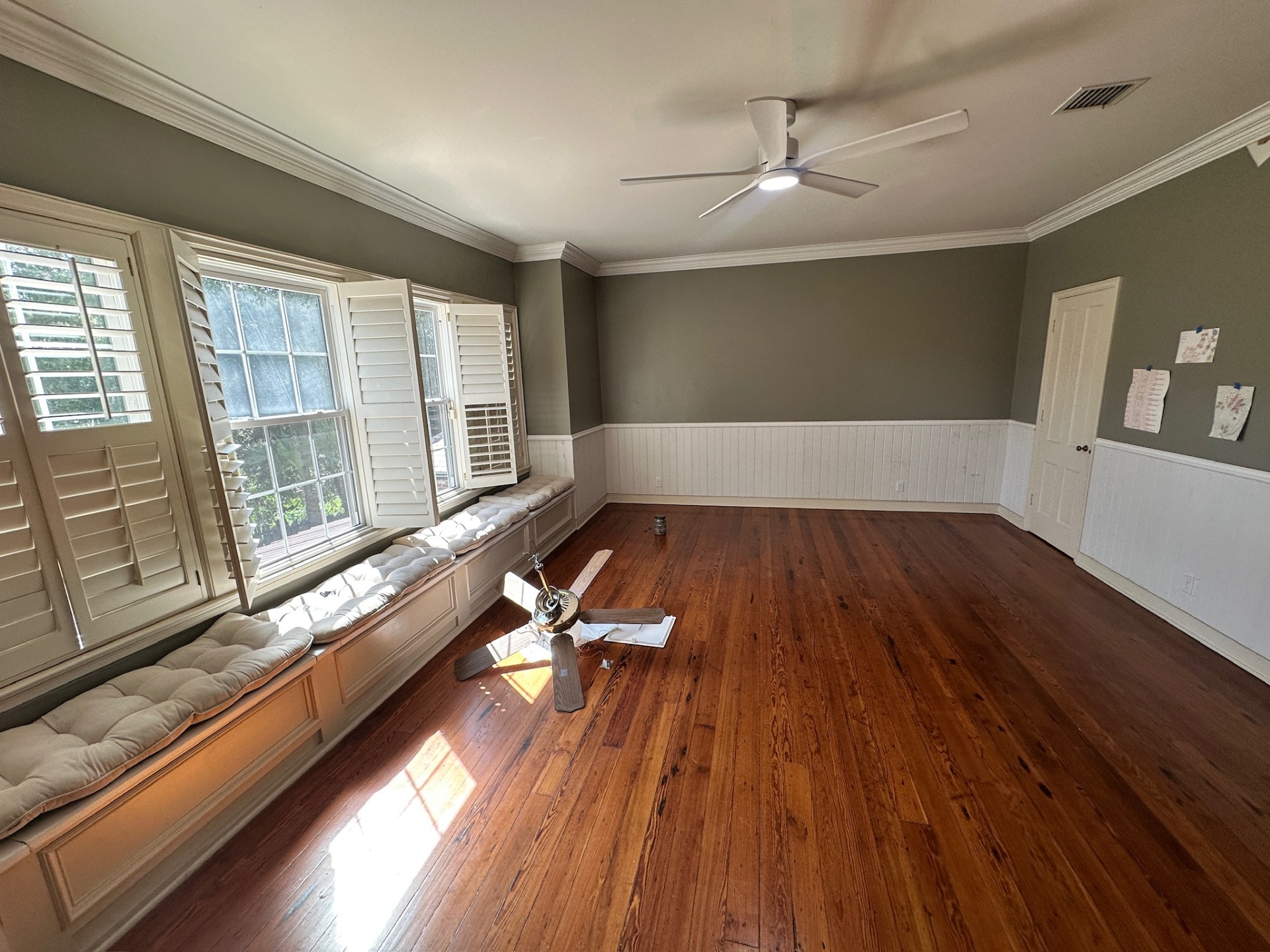 Long run of custom beadboard wainscoting alongside a built-in cushioned window seat under plantation shutters in a Covington Louisiana bedroom