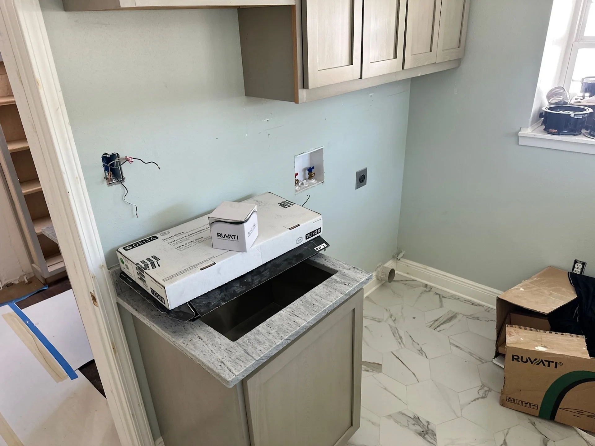 Wet bar area at Blanke Street Metairie home during finish phase with hex marble floor tile, new granite countertop, undermount sink cutout, and Delta faucet plus Ruvati sink boxes on the counter