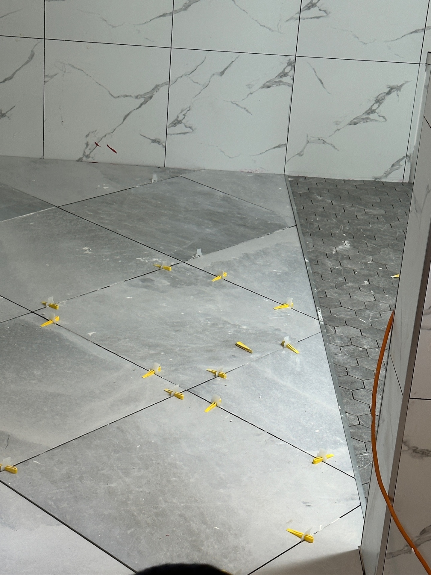 Floor transition detail between large-format porcelain and hex mosaic shower floor in Metairie master bath