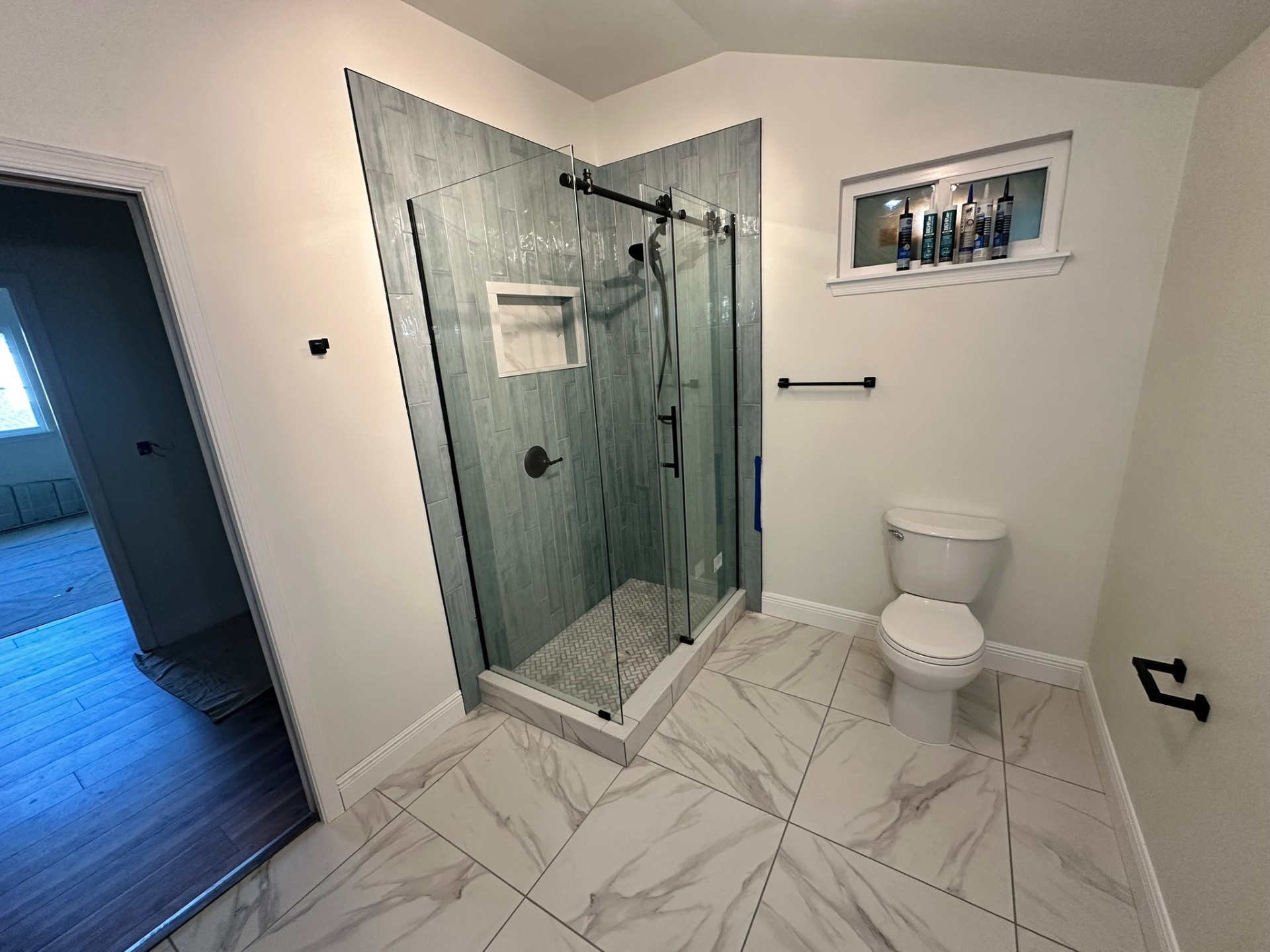 Finished vaulted master bathroom in Metairie second-floor addition with gray vertical tile shower, herringbone mosaic shower floor, marble-look porcelain tile floor, matte black sliding glass door, niche and toilet