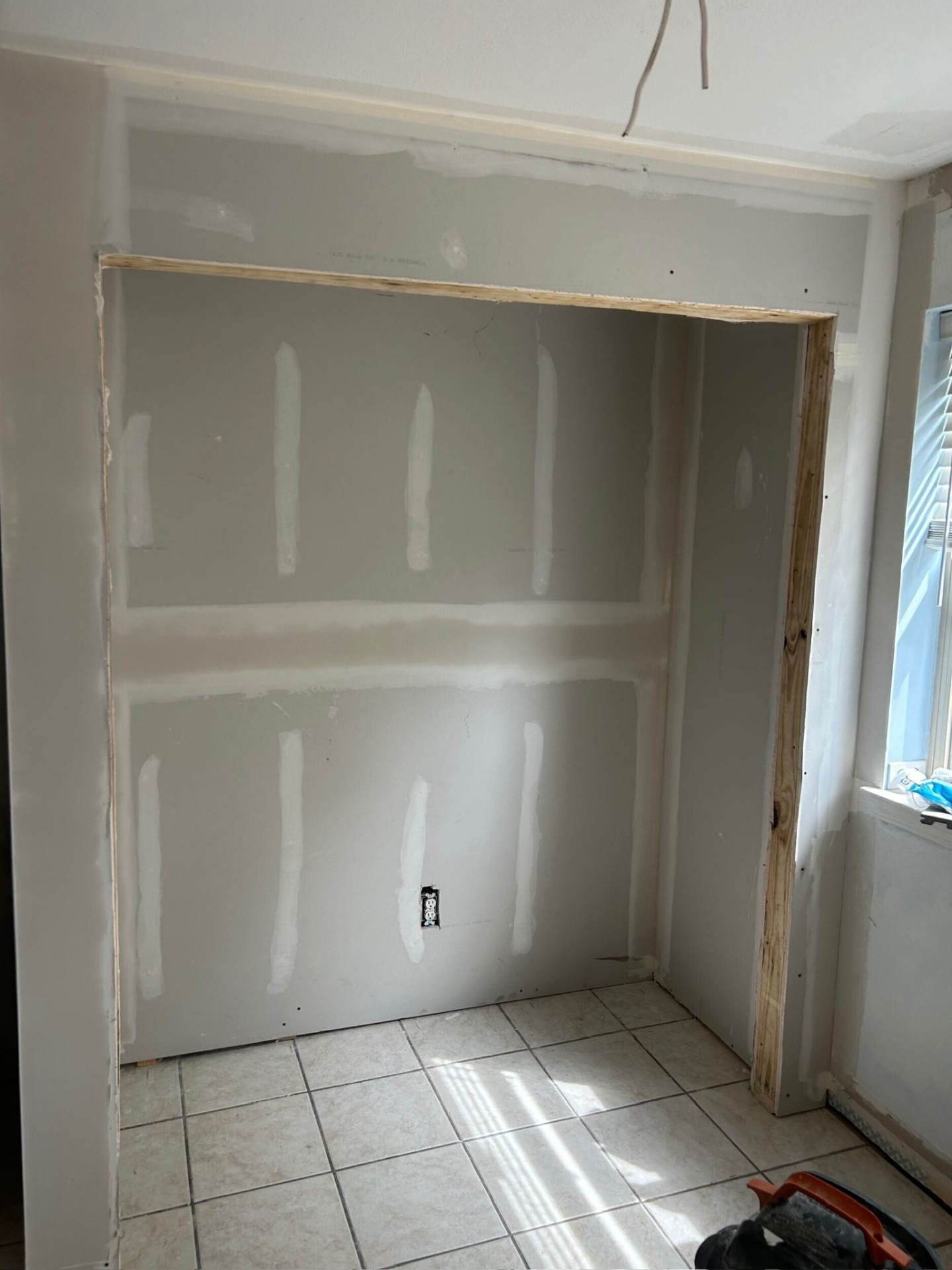 New second-floor closet opening on the Metairie addition with drywall hung and seams taped inside the framed opening, exposed pine jamb edges and original first-floor tile floor visible below