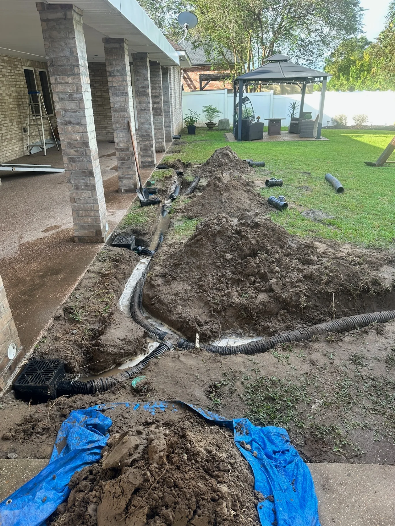 Drainage trench dug along rear of Destrehan Louisiana home with corrugated pipe and catch basins being installed for hidden downspout system by Cajun Home Services