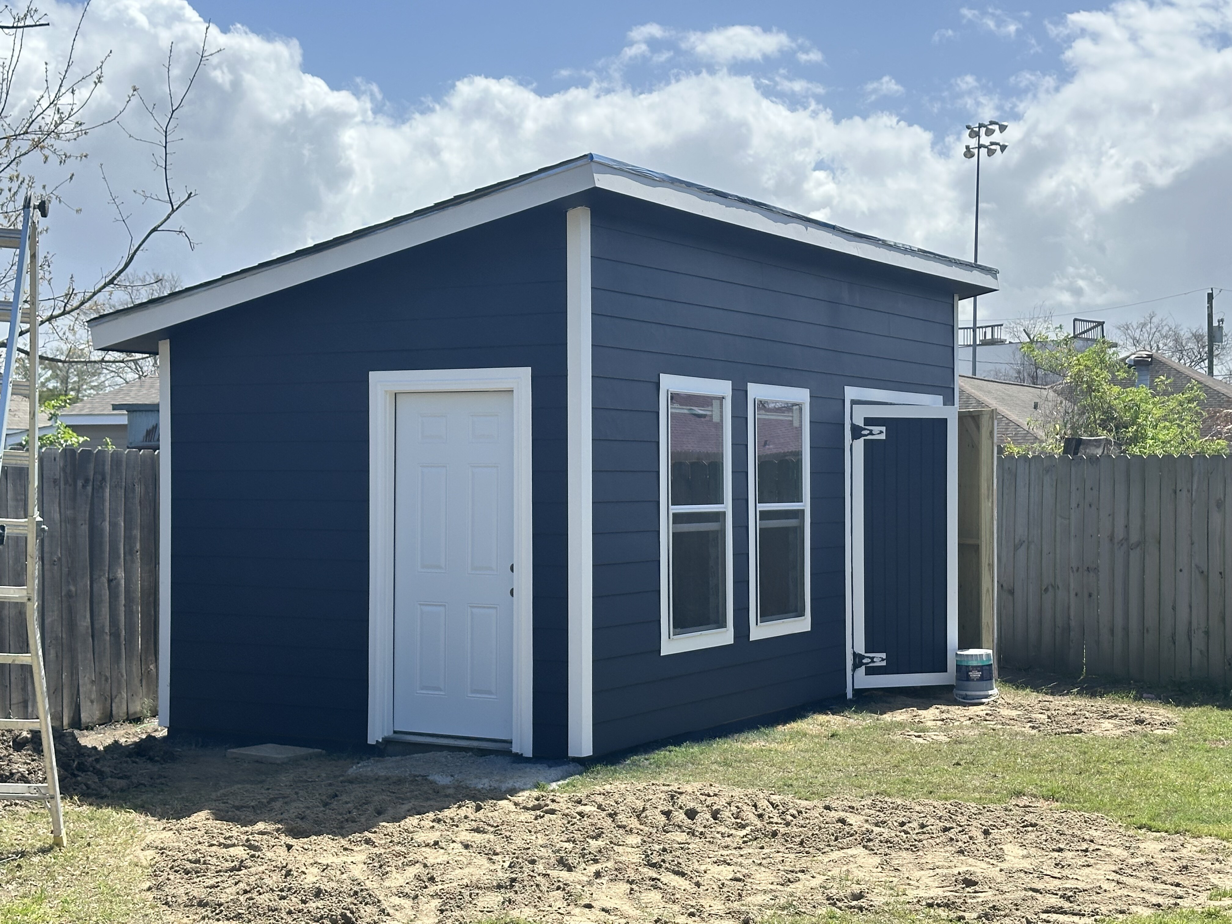 Interior of Metairie Hardie-siding shed mid-build, viewed through finished door opening with materials staged inside