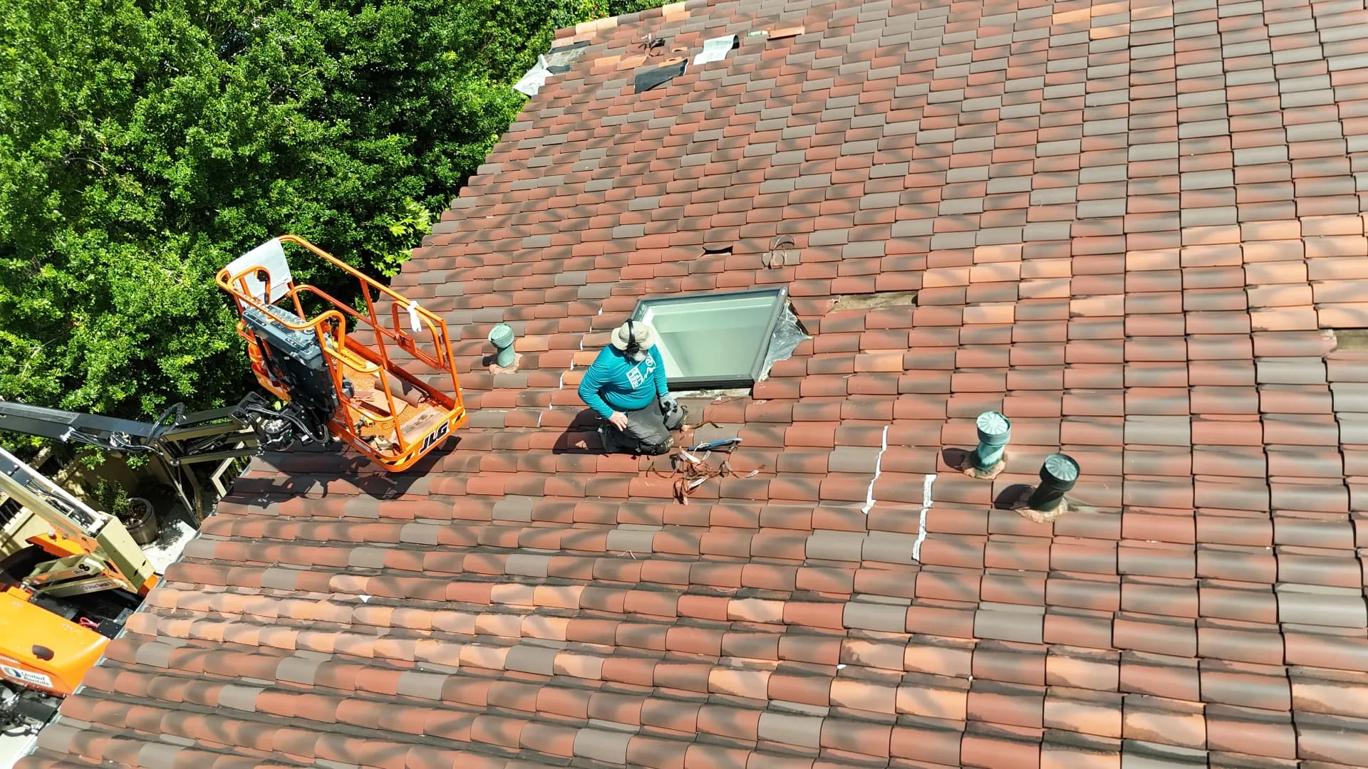 Aerial view of a Cajun Home Services roofer setting replacement terra cotta tiles and sealing the skylight on a Metairie Louisiana home