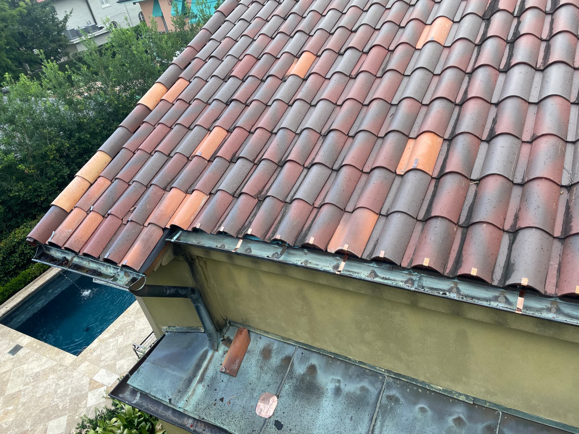 Completed terra cotta tile roof edge above a pool with re-secured copper gutter in Metairie Louisiana