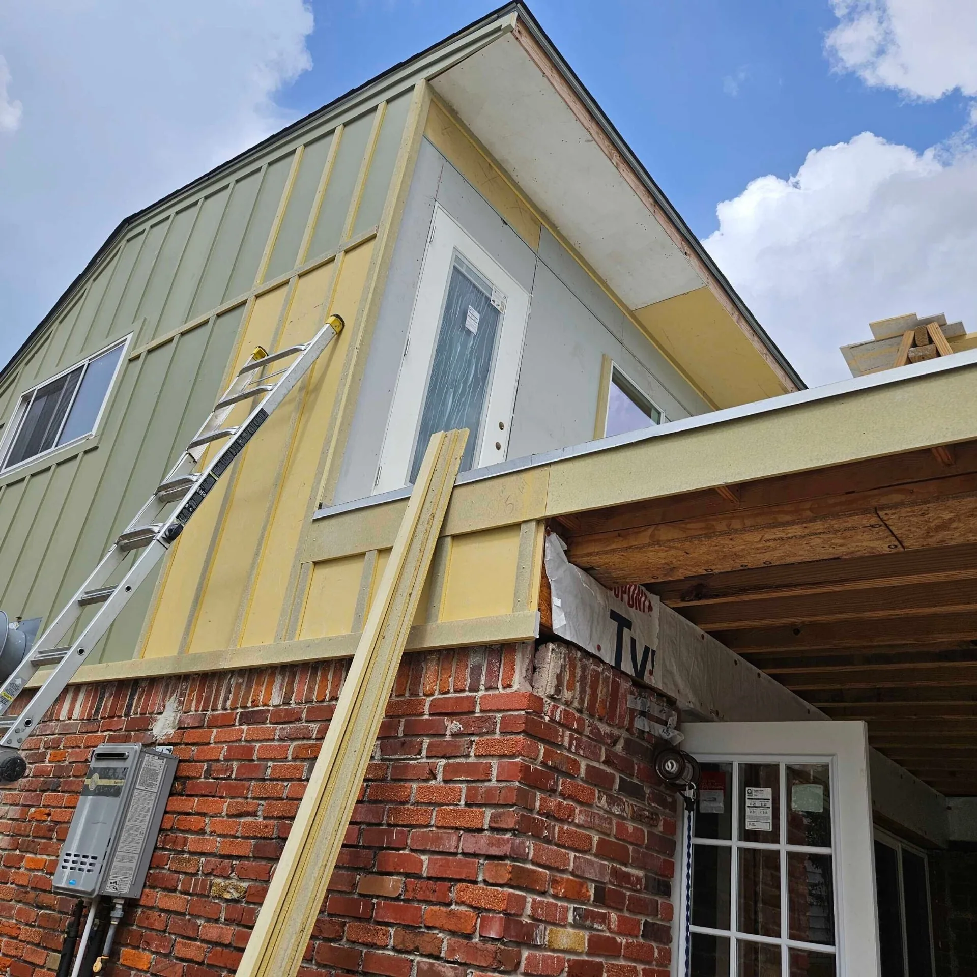 Side gable of new second-story addition at Blanke Street Metairie home showing exterior door and board-and-batten siding in primer over the existing brick first floor