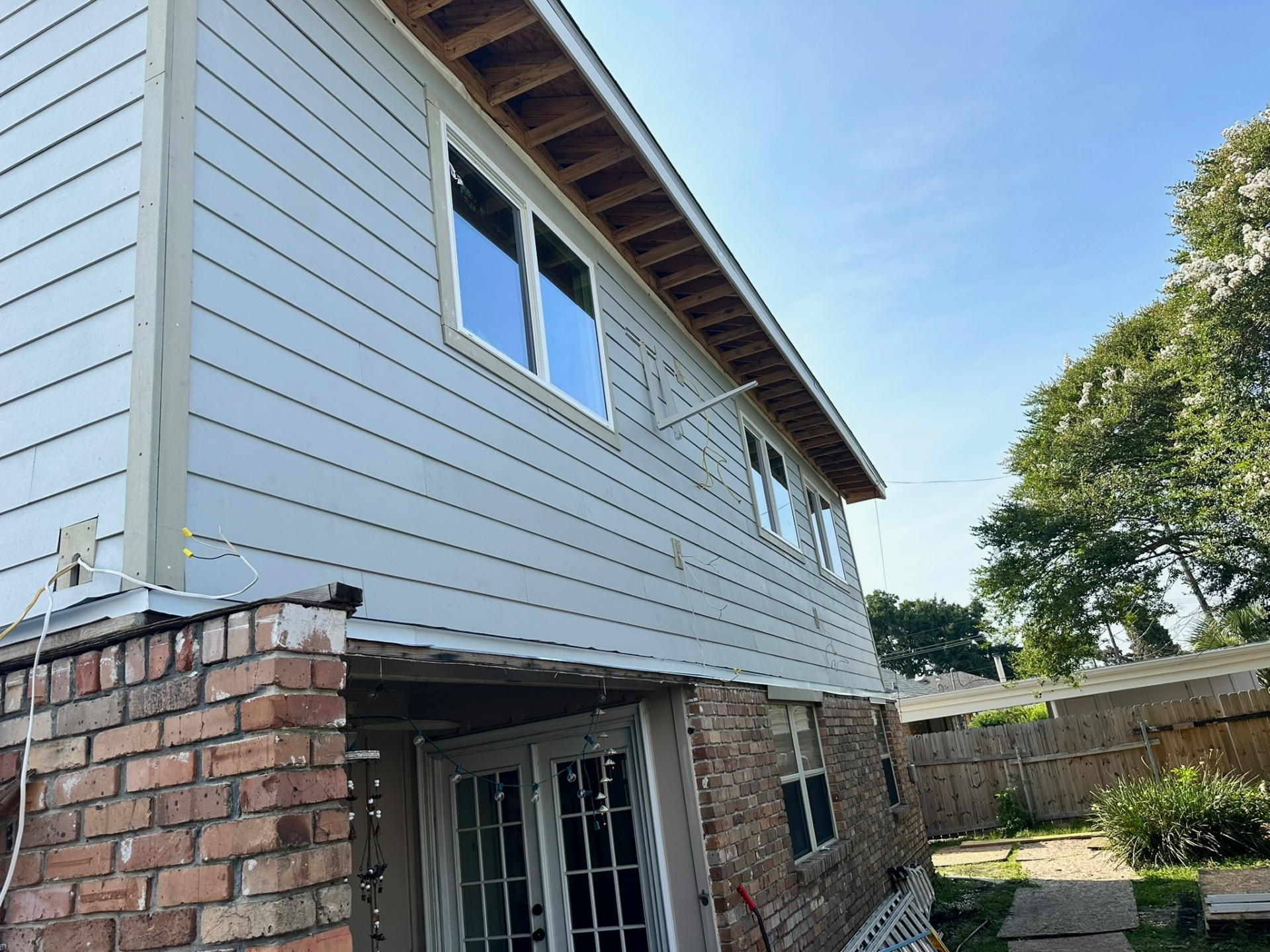 Rear-side elevation of the Metairie second-floor addition with new window band and Hardie lap siding installed, photographed from the covered patio corner