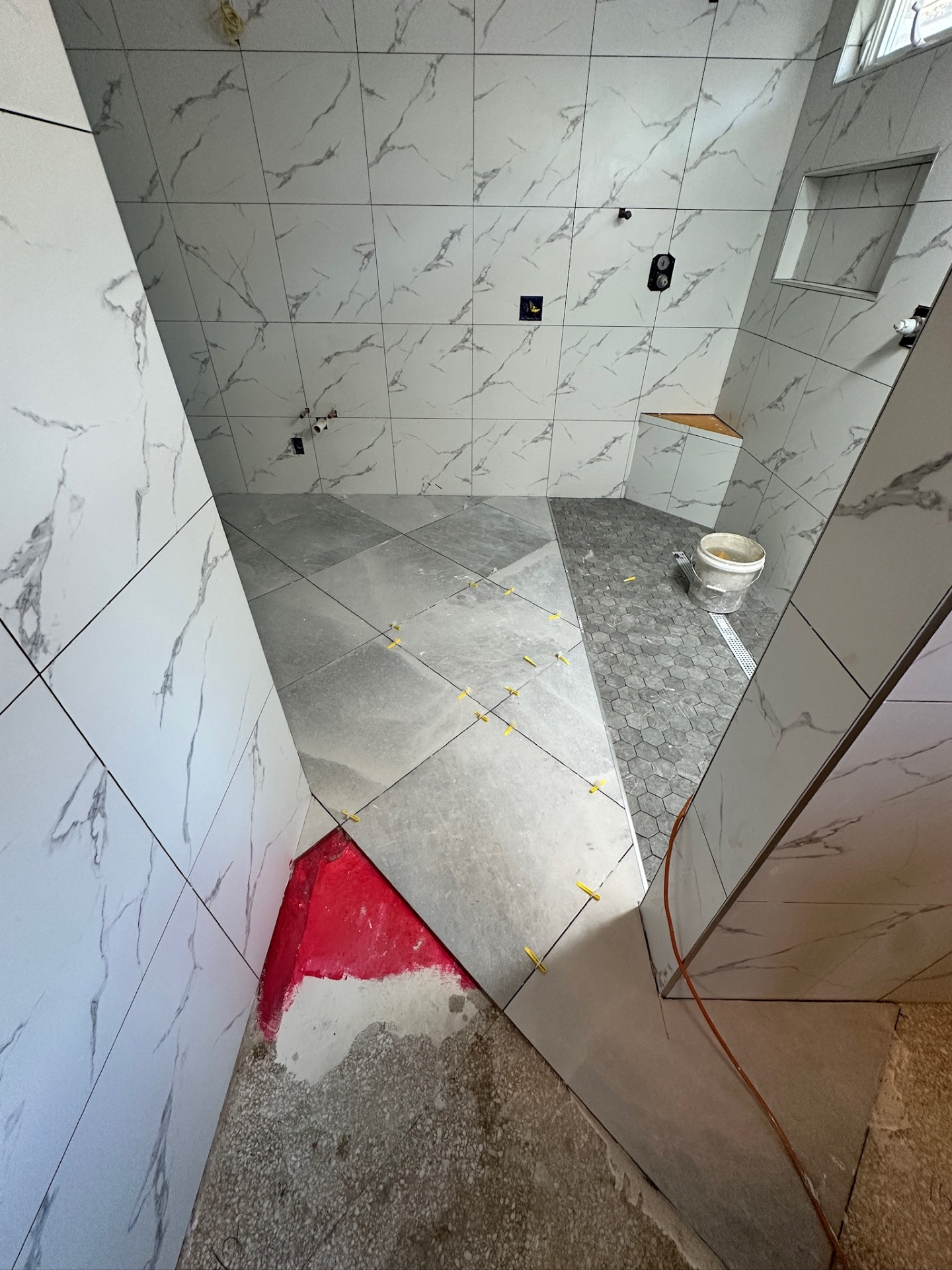 Floor tile going down with a pink RedGard patch at the threshold in Metairie master bath